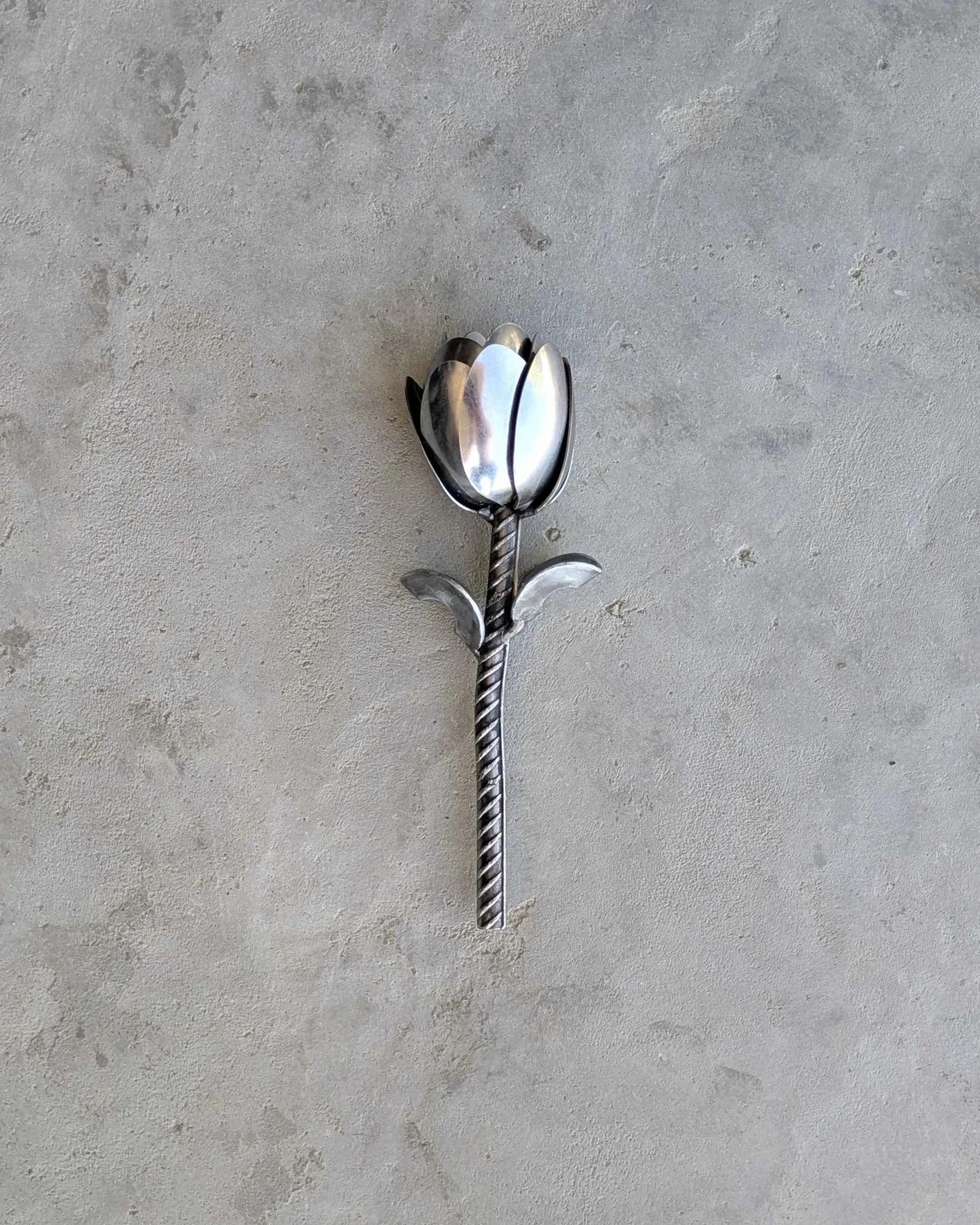 A metal art tulip made from spoons, rebar and washers, sitting on concrete.