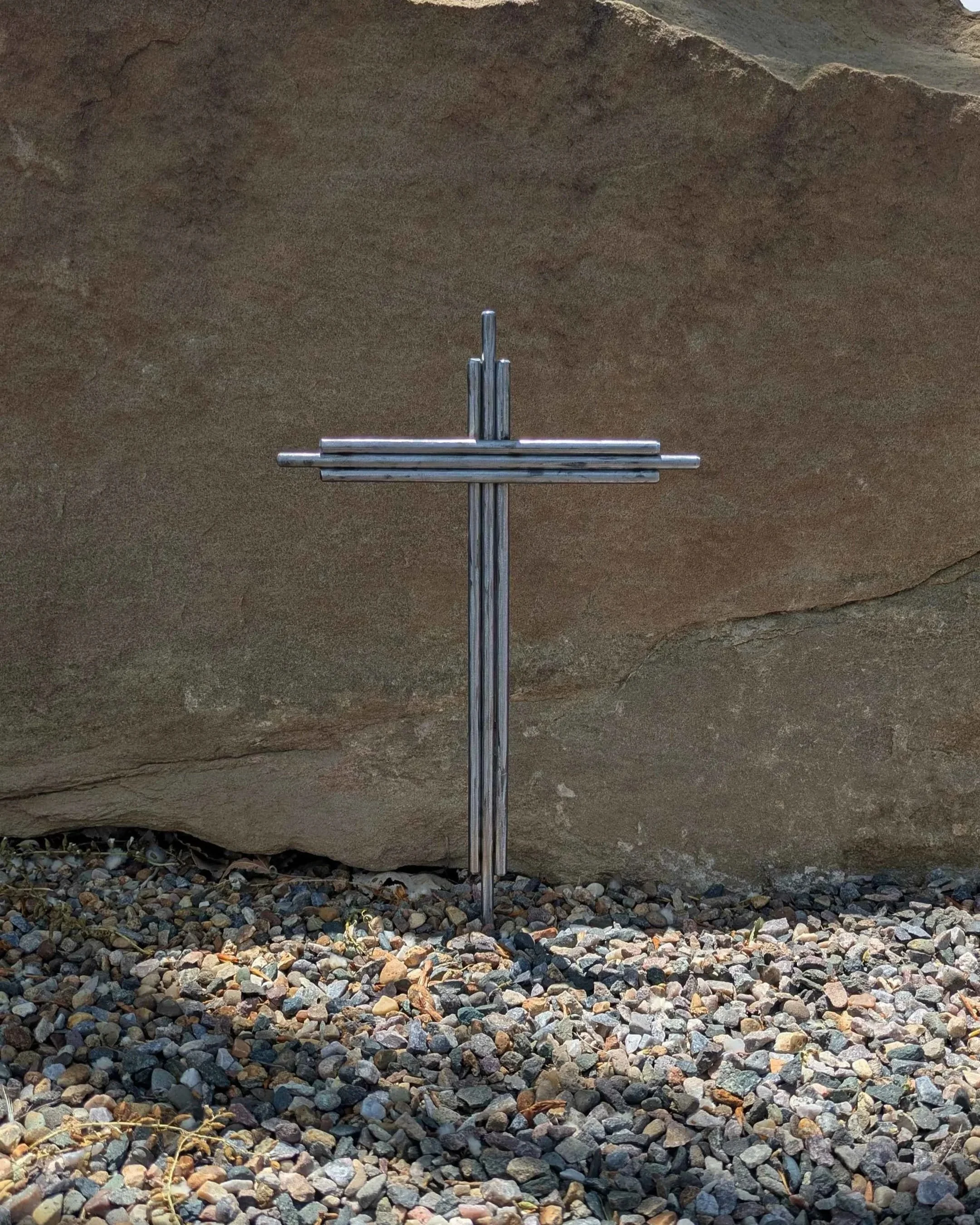 A metal art cross made from pieces of thick polished metal rod, driven into the ground as a yard decoration