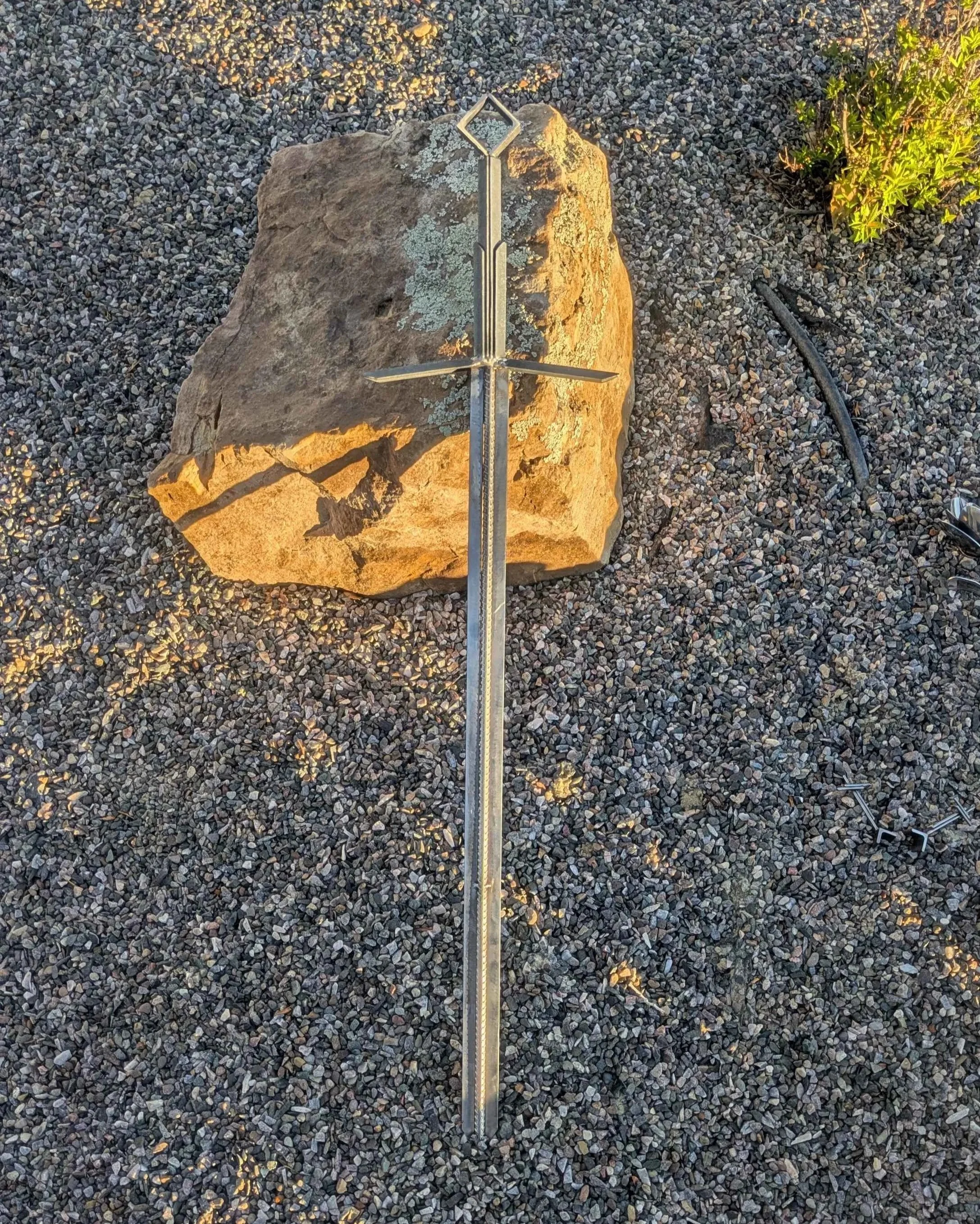A metal art sword made from industrial style materials, leaning against a rock.