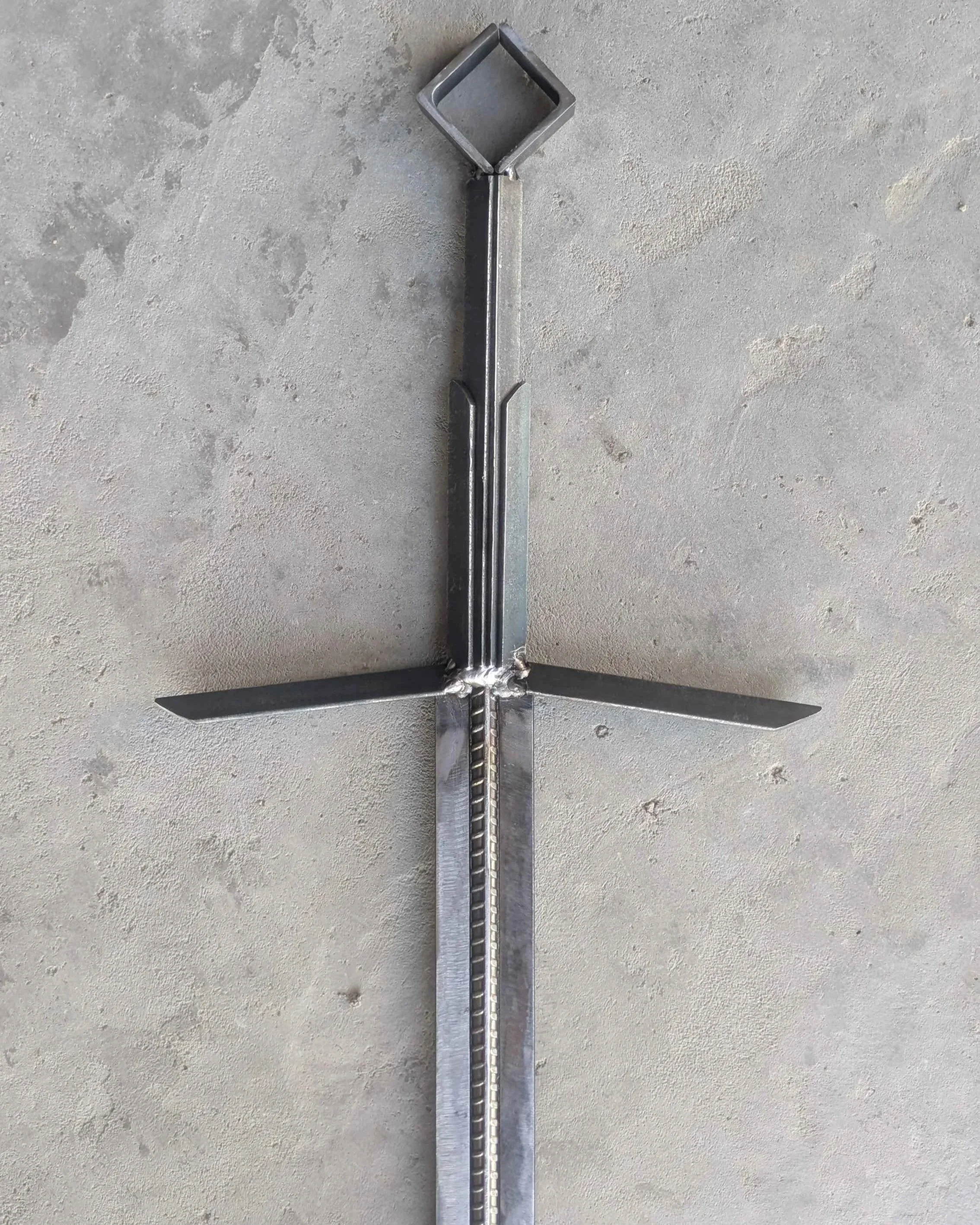 The hilt of a metal art sword made from industrial style materials, laying upon a slab of concrete.
