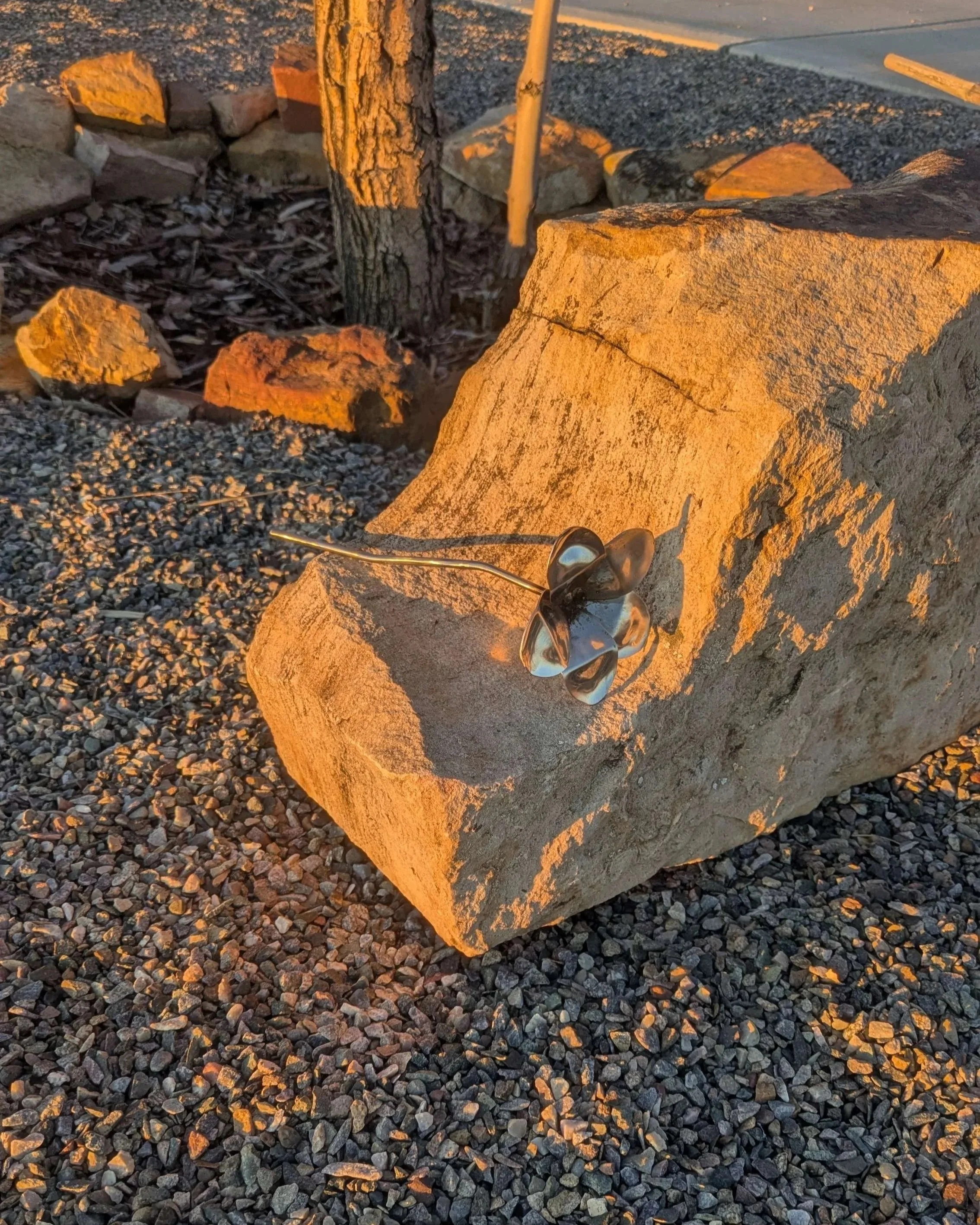 A metal art flower made from bent spoon heads and metal rod sitting upon a rock..