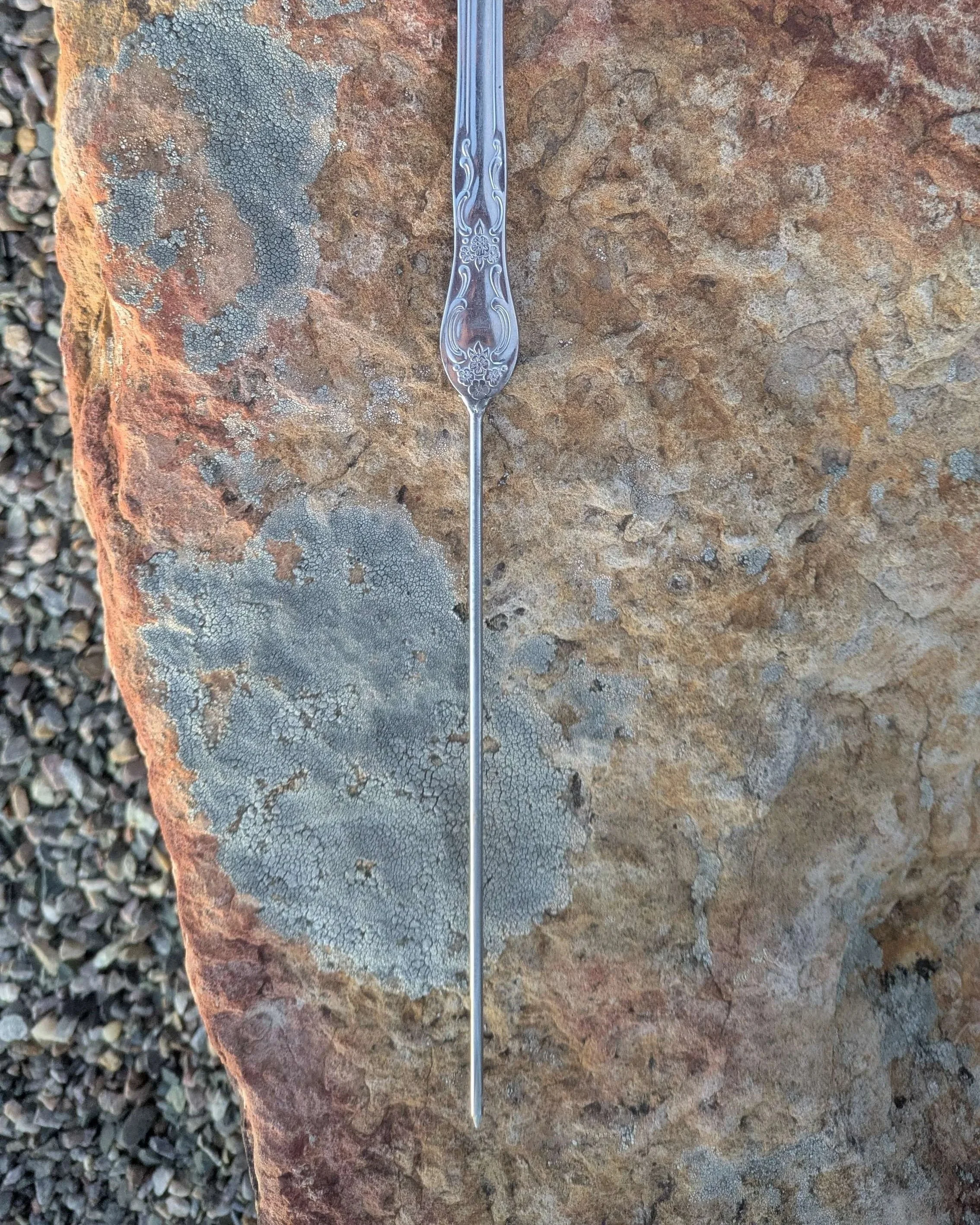 The base of a handmade silverware cross, a metal spike attached to the end for planting in a yard.