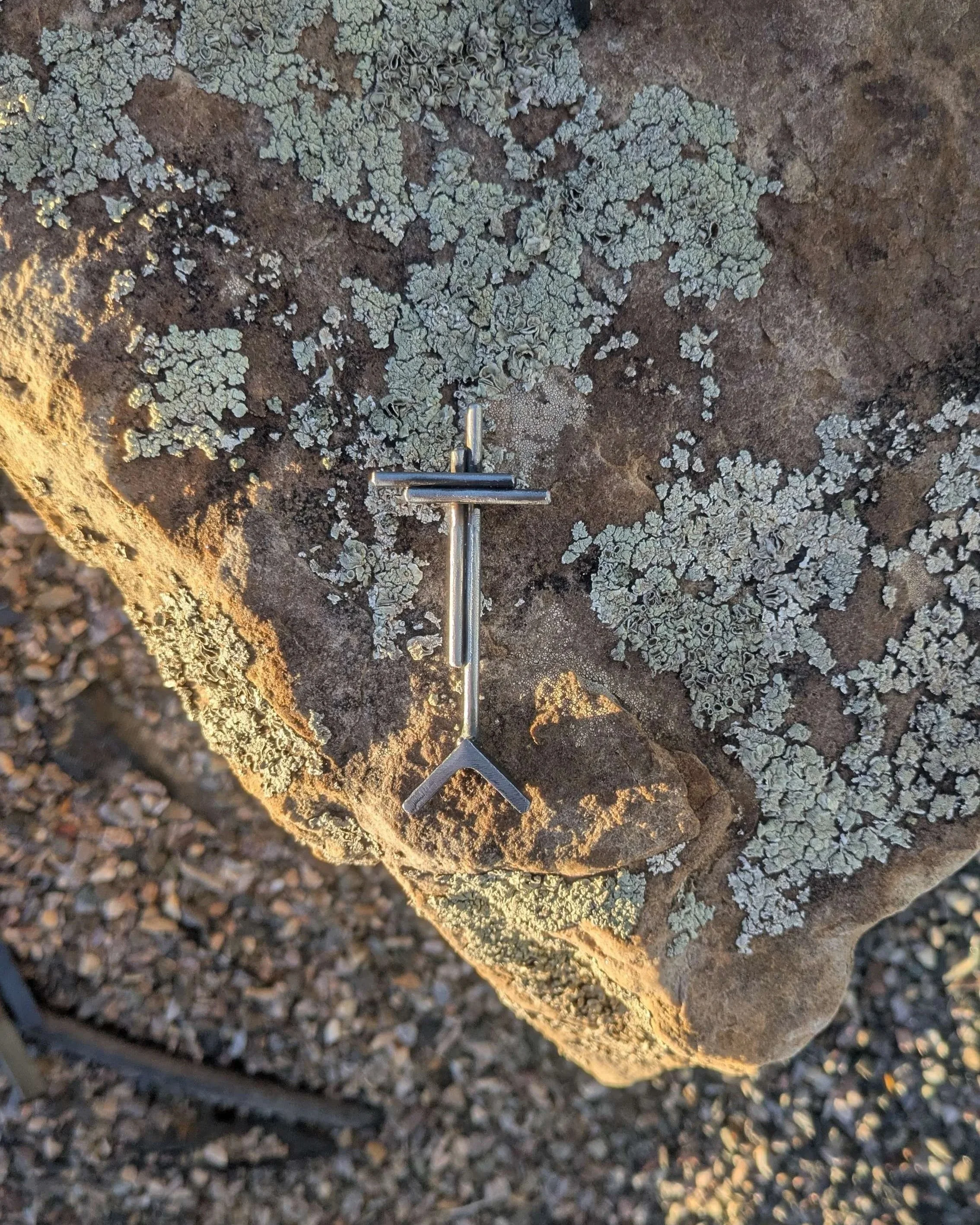 A small welded metal cross sitting upon a rock, a small gift for someone's desk.