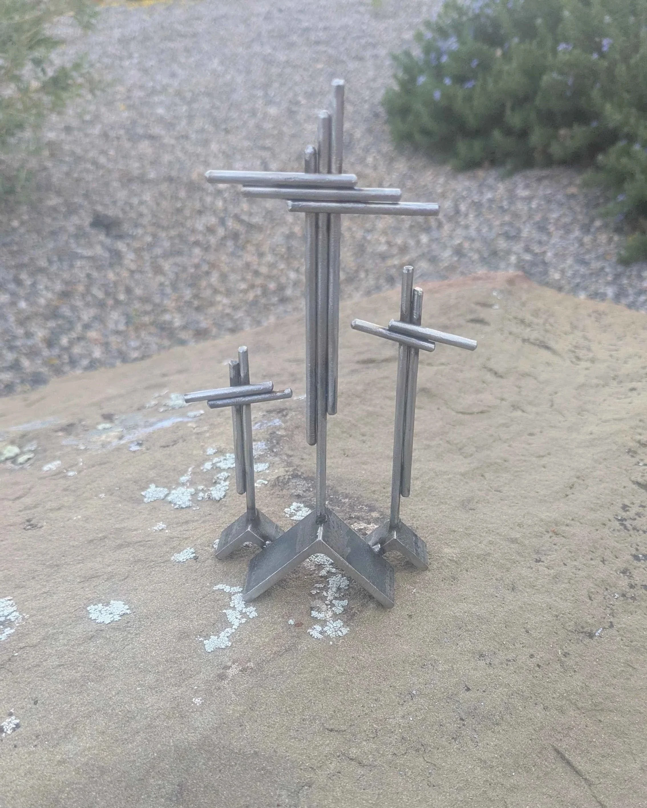 A metal art display of three crosses on three hills, made from rods and angle iron.