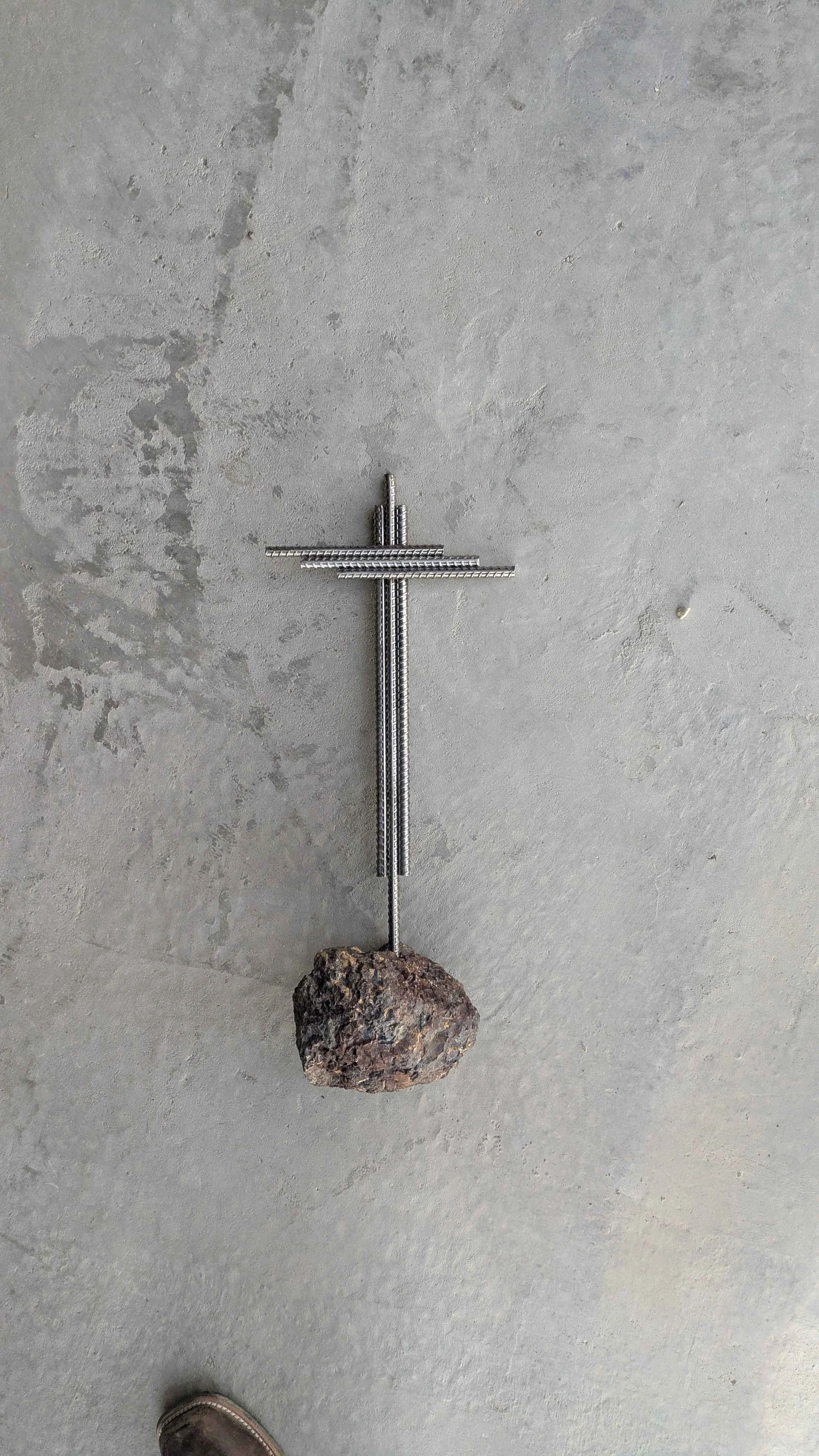 A metal art cross made from rebar planted in stone as a yard decoration.