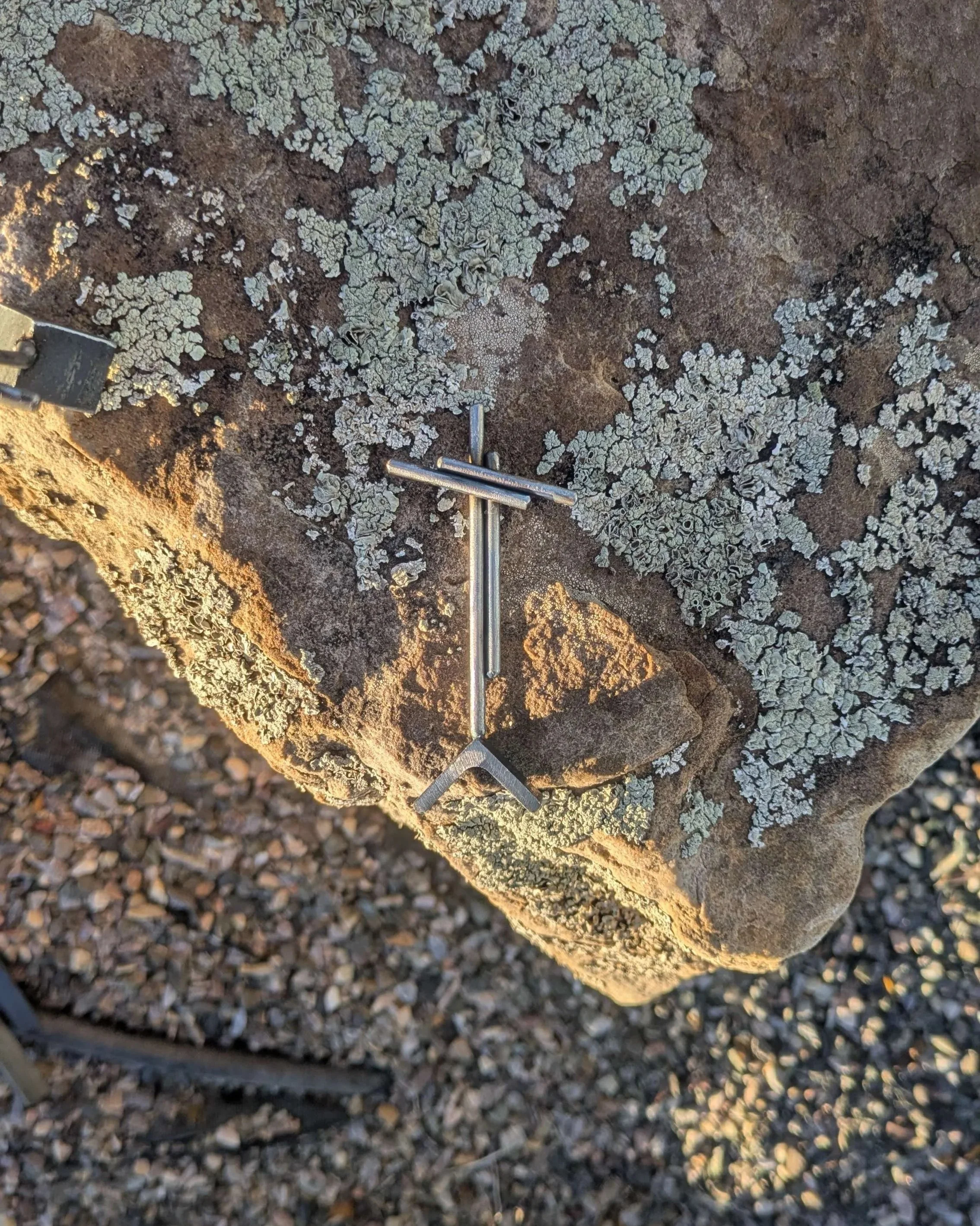 A small welded metal cross sitting upon a rock, a small gift for someone's desk.