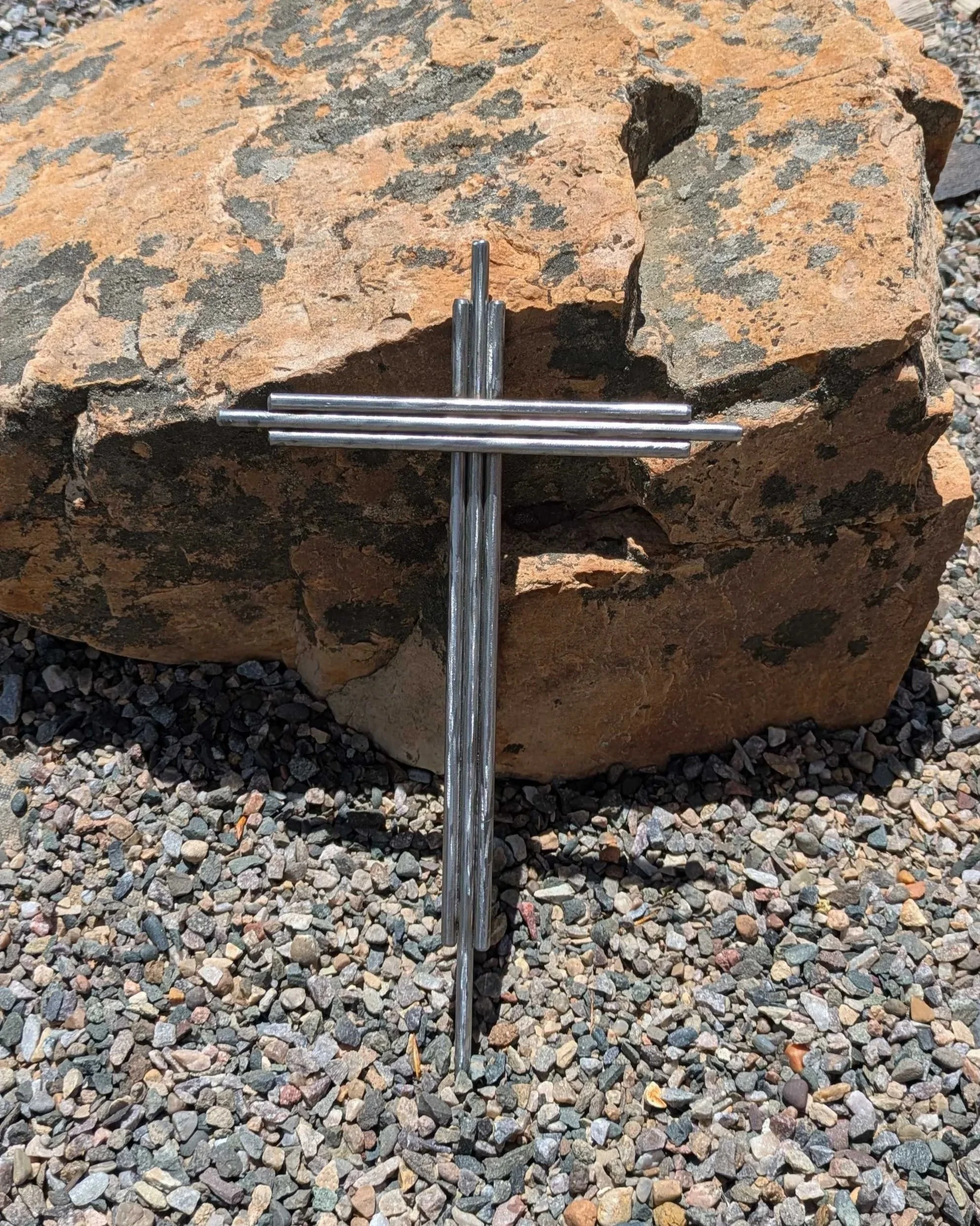 A metal art cross made from pieces of thick polished metal rod, driven into the ground as a yard decoration