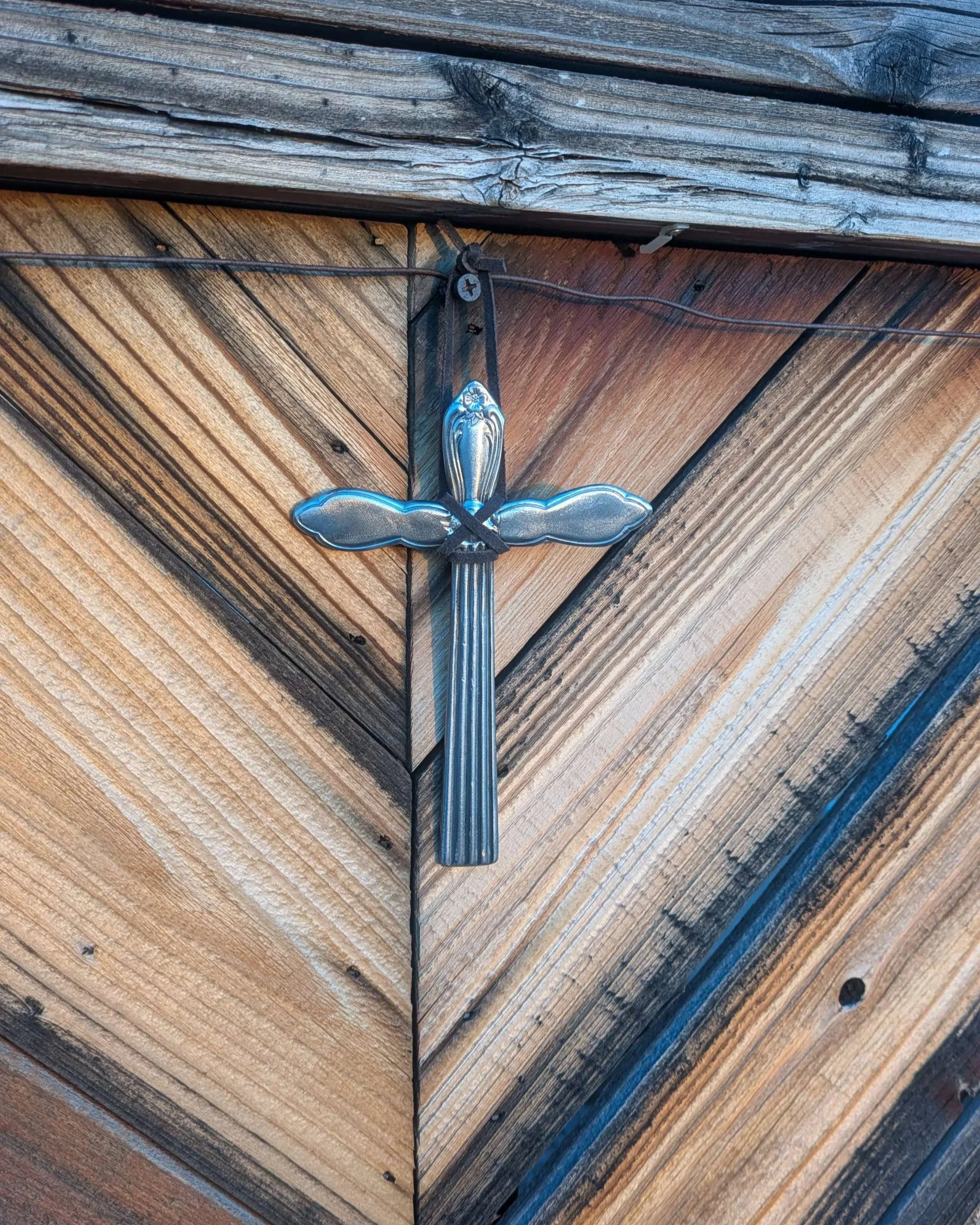 A metal art silverware cross with a black leather hanging strap.