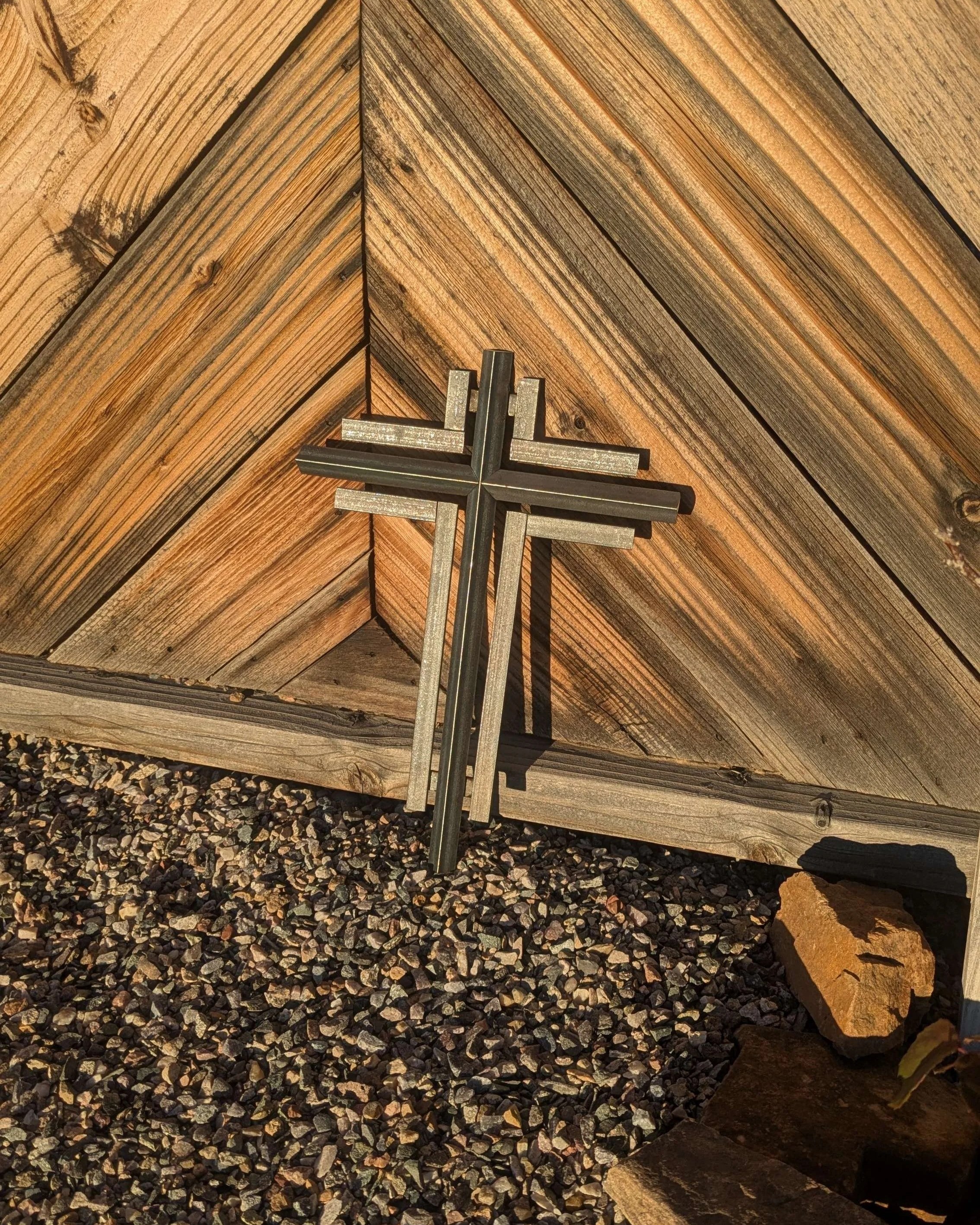 A metal art cross sculpture leaning against a wooden fence.