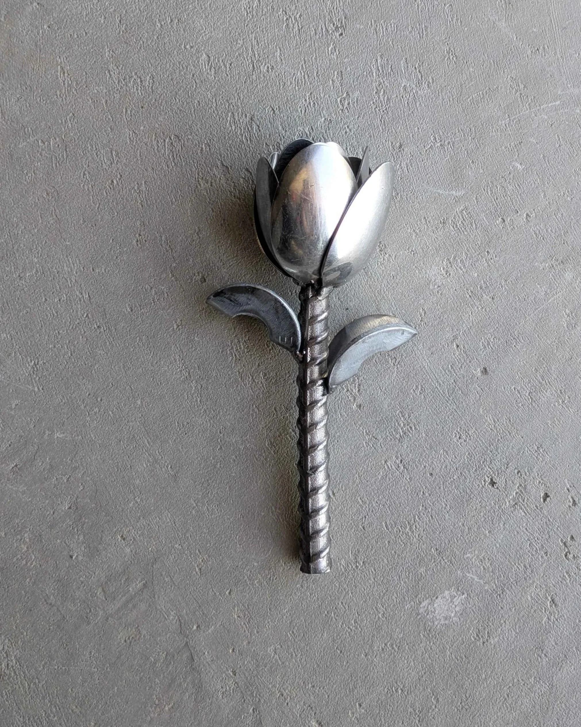 A metal art tulip made from spoons, rebar and washers, sitting on concrete.
