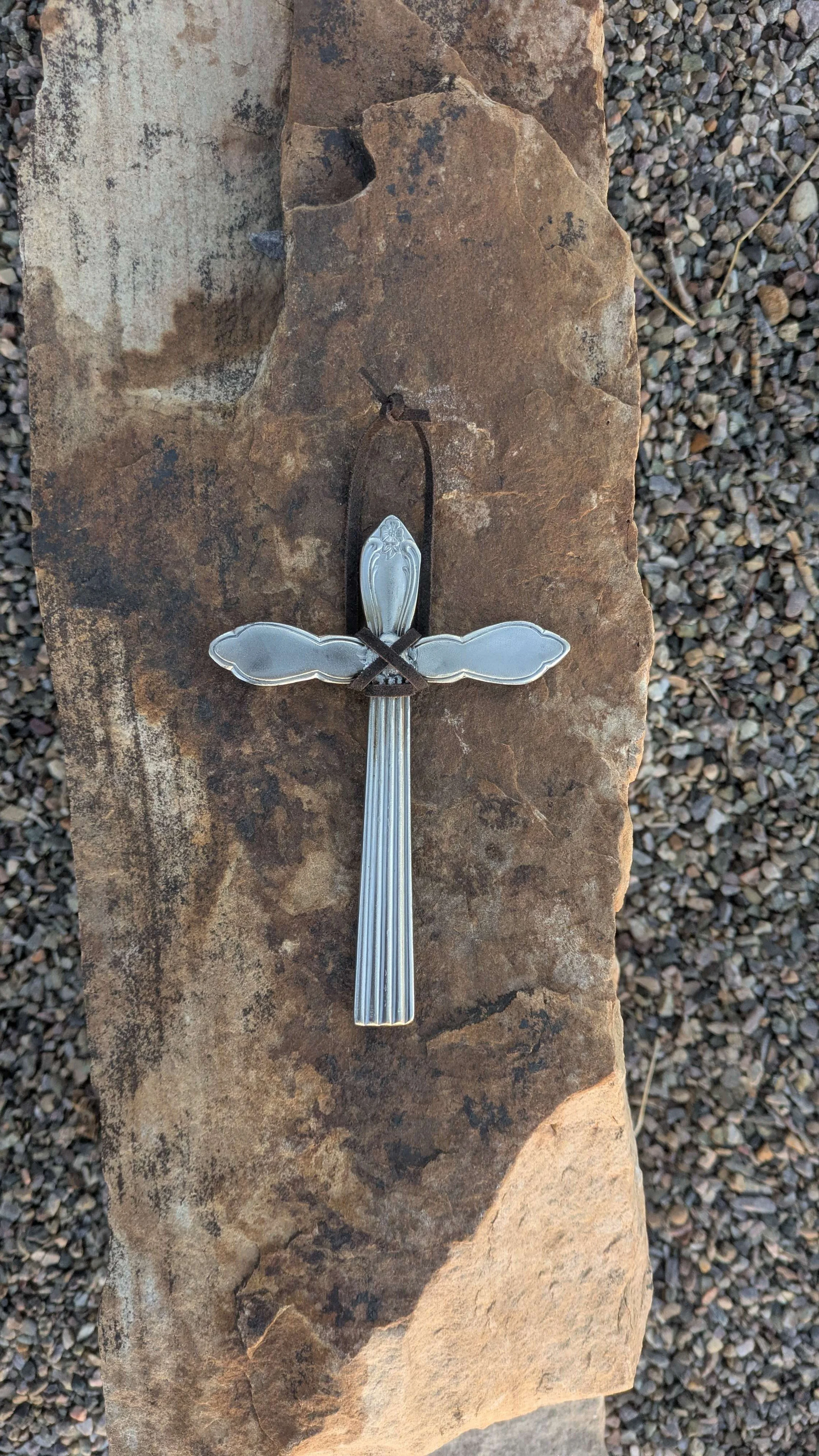 A metal art silverware cross with a black leather hanging strap.