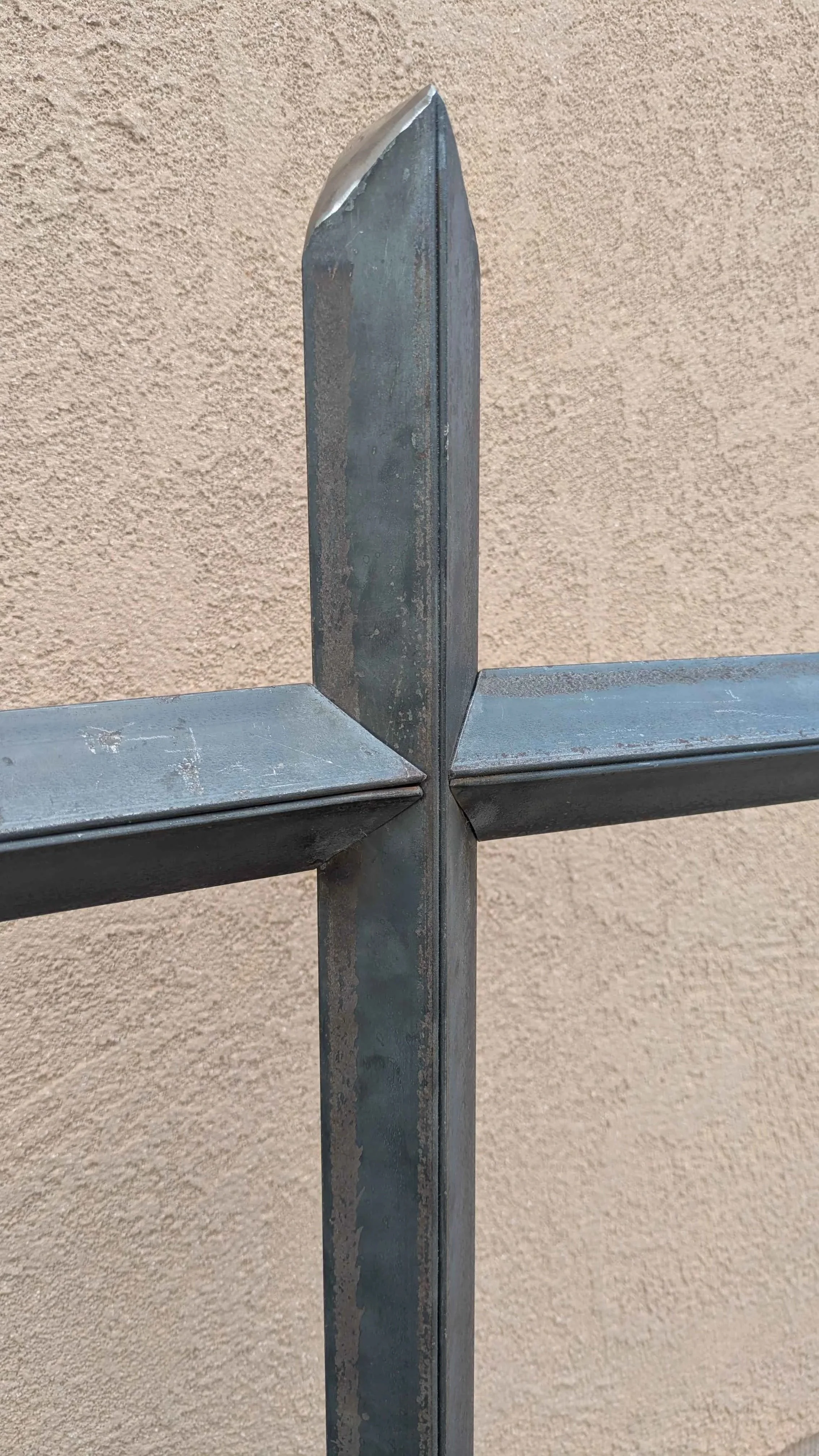 A closeup of a large metal art cross sculpture made from carefully layered angle iron, designed to be a yard decoration.