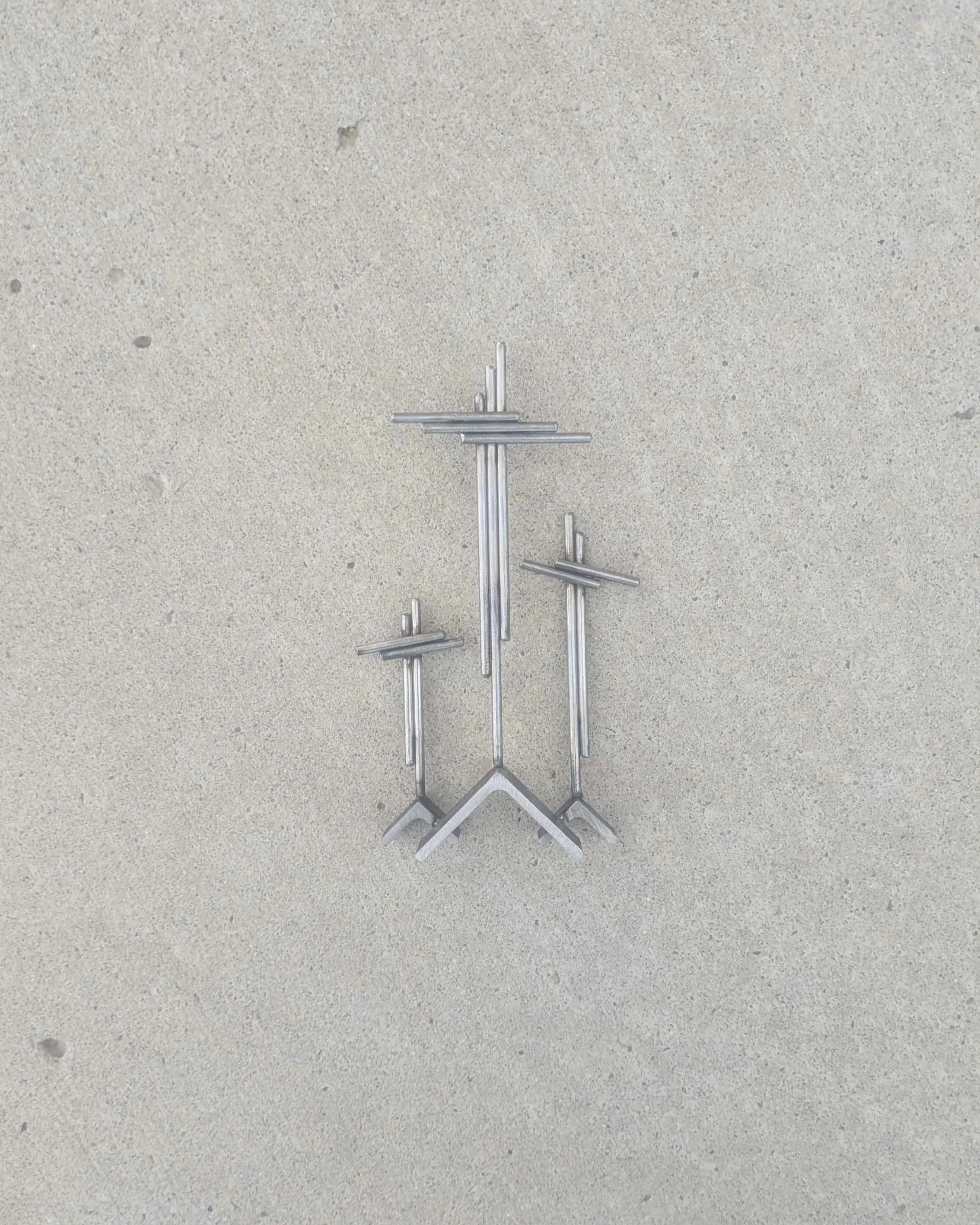 A metal art display of three crosses on three hills, made from rods and angle iron.