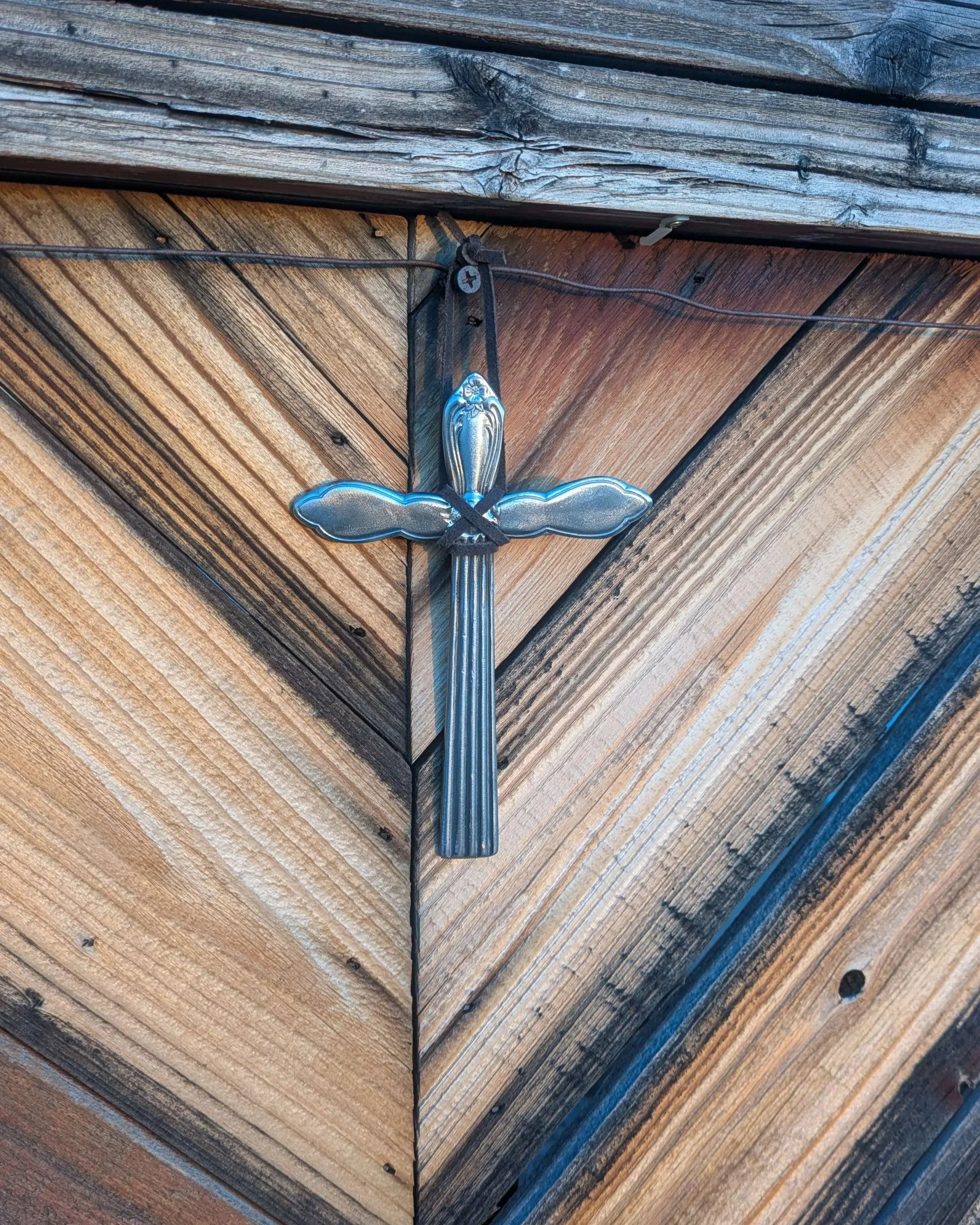 A metal art silverware cross with a leather hanging strap.
