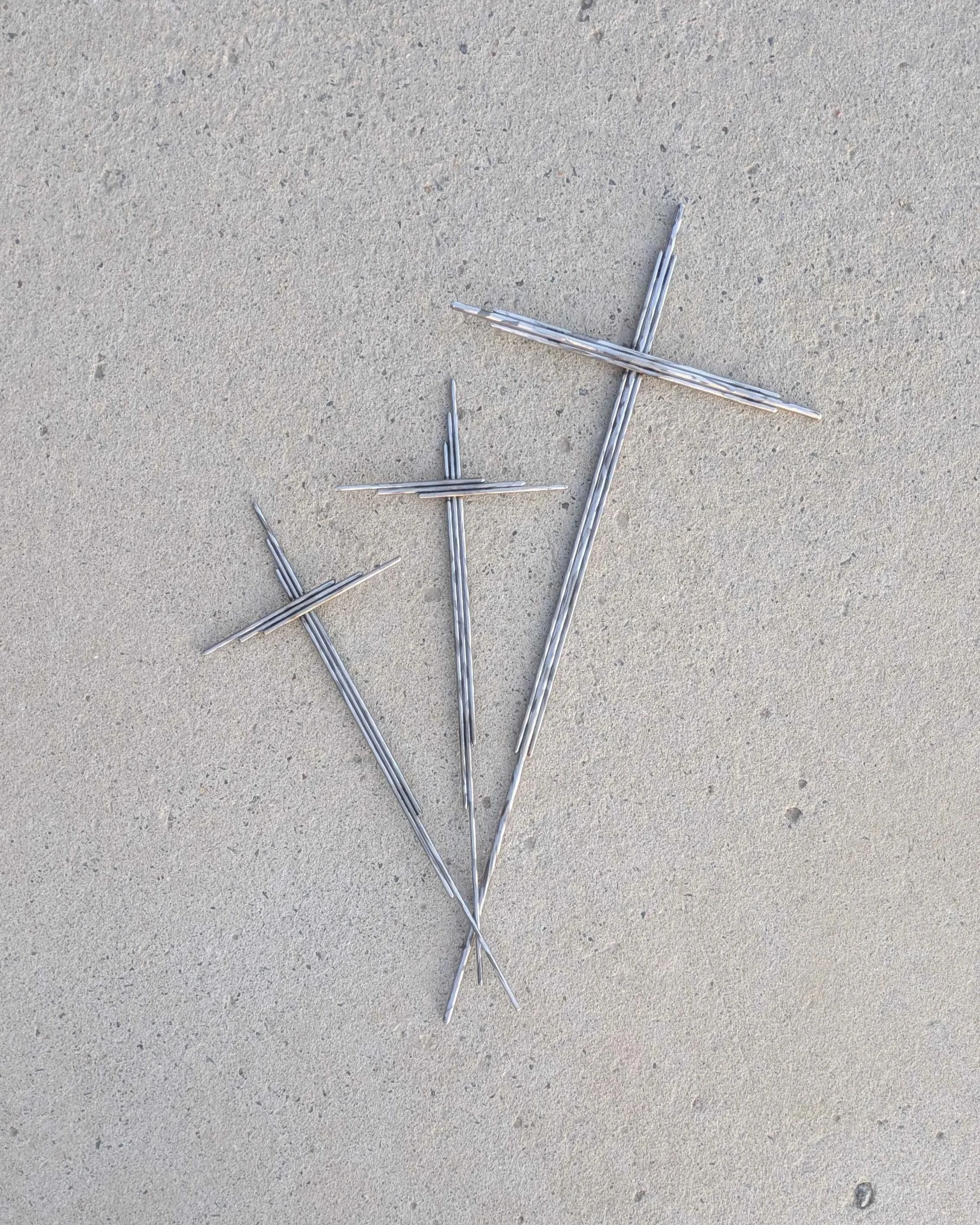 A large metal art cross made from long pieces of polished metal rod, with a long spike on the end for planting in a front yard.