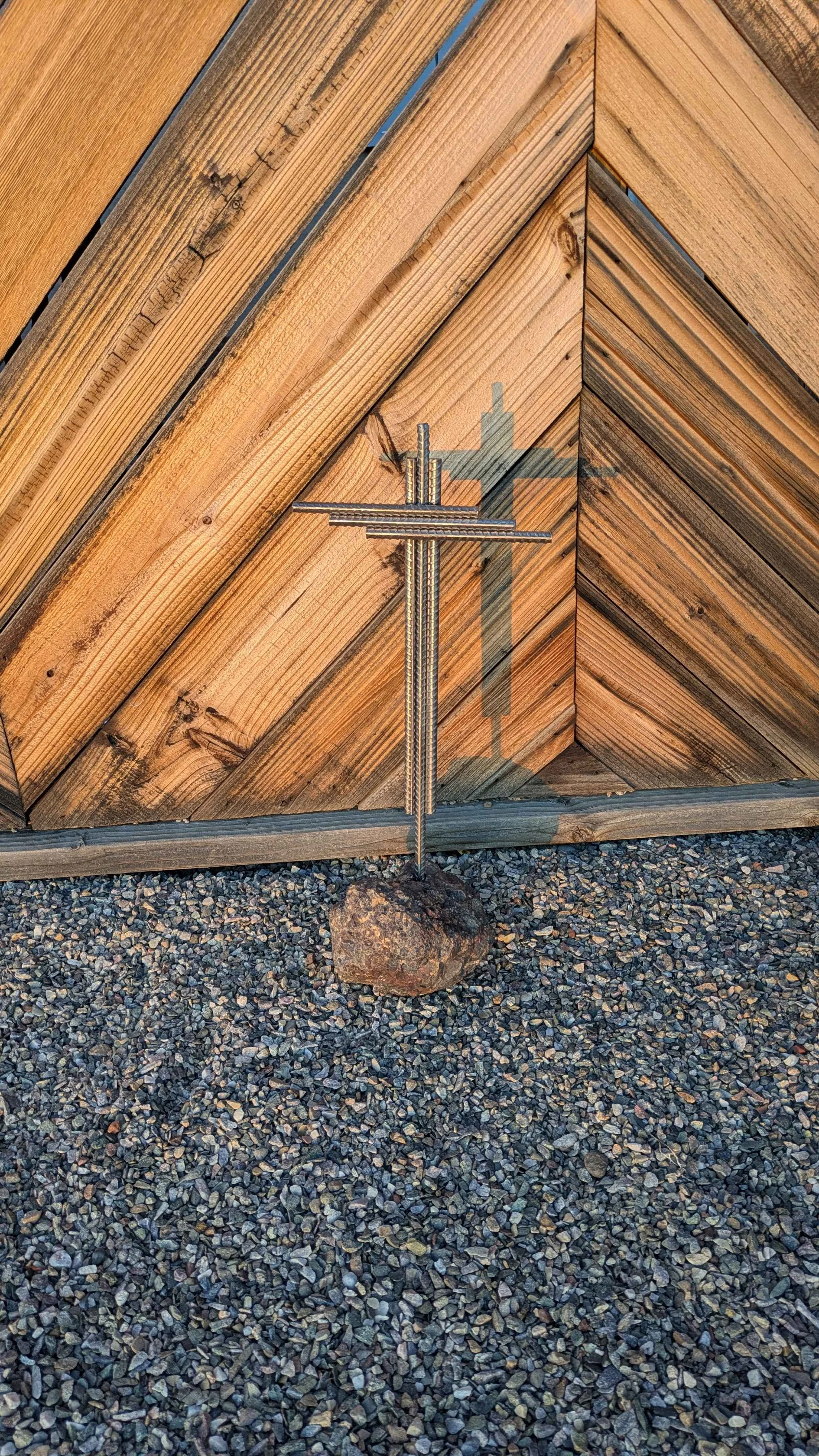 A metal art cross made from rebar planted in stone as a yard decoration.