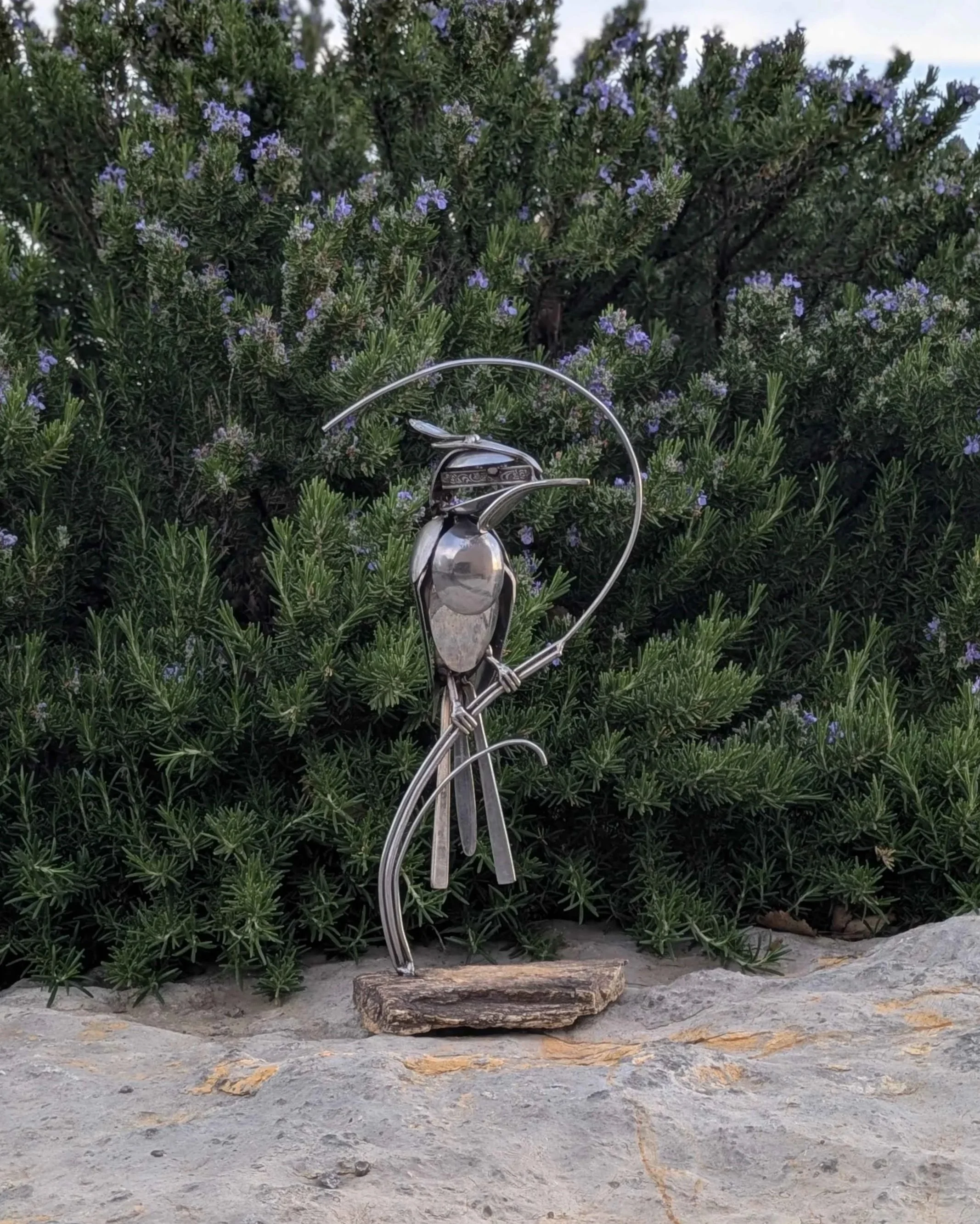 A metal sculpture of a woodpecker made from silverware attached to a petrified wood base.