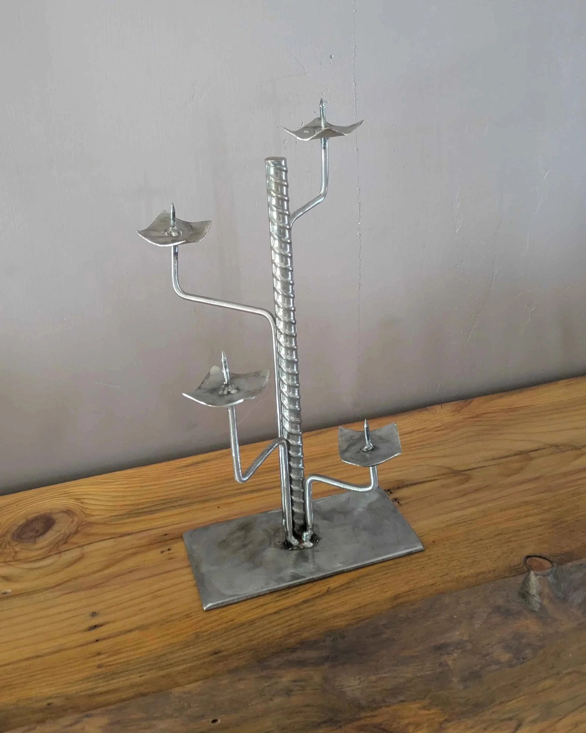 A metal art industrial style candleholder made from rebar and plate steel sitting on a shelf.