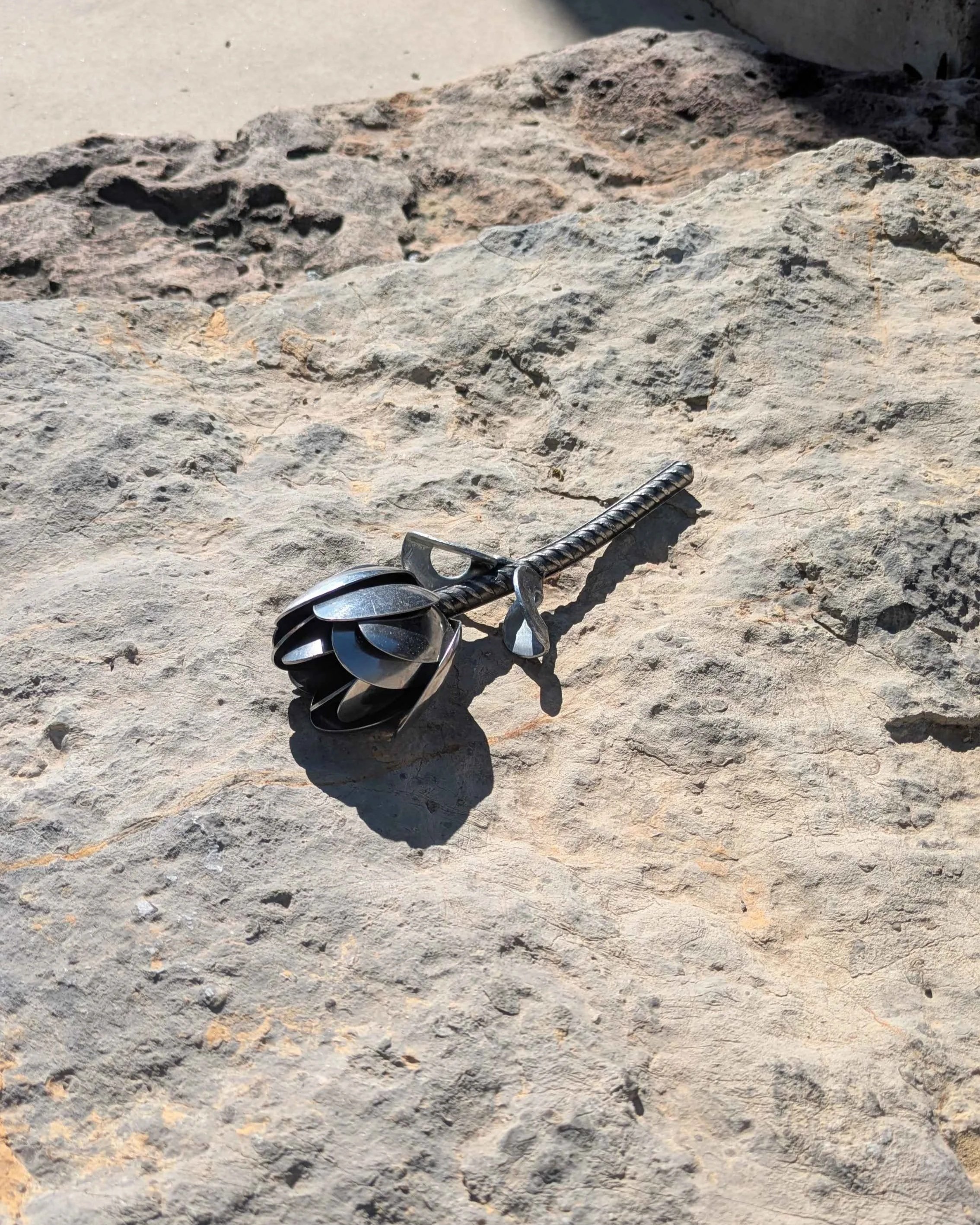 A metal art tulip made from spoons, rebar and washers, sitting on a rock.