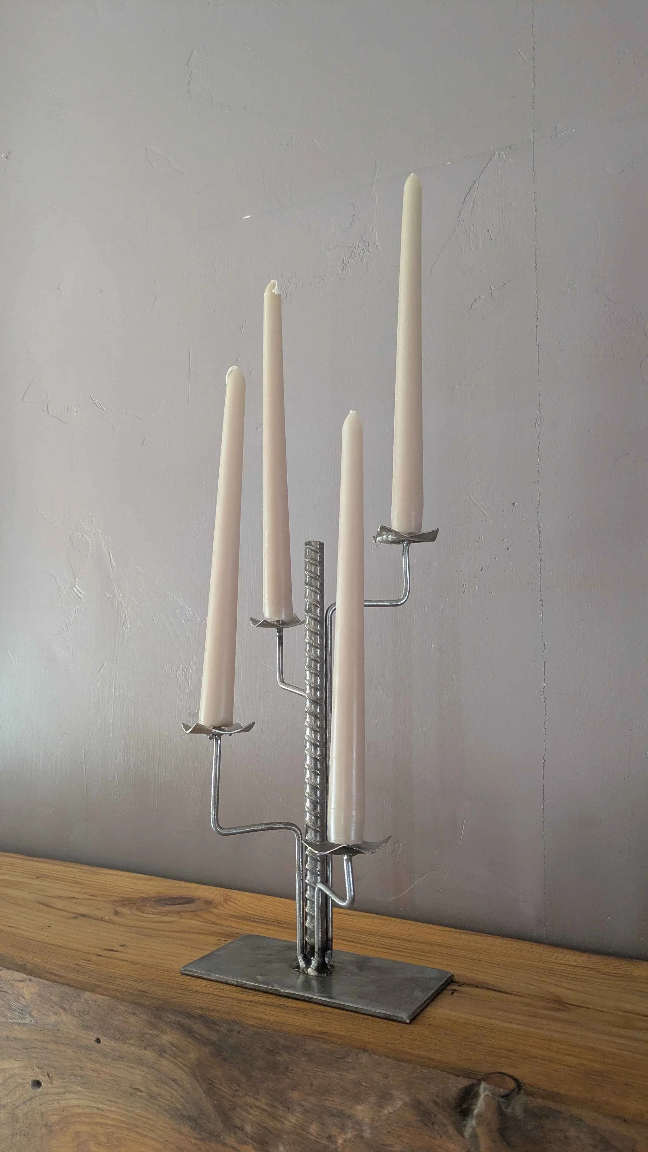 A metal art industrial style candleholder made from rebar and plate steel sitting on a shelf.