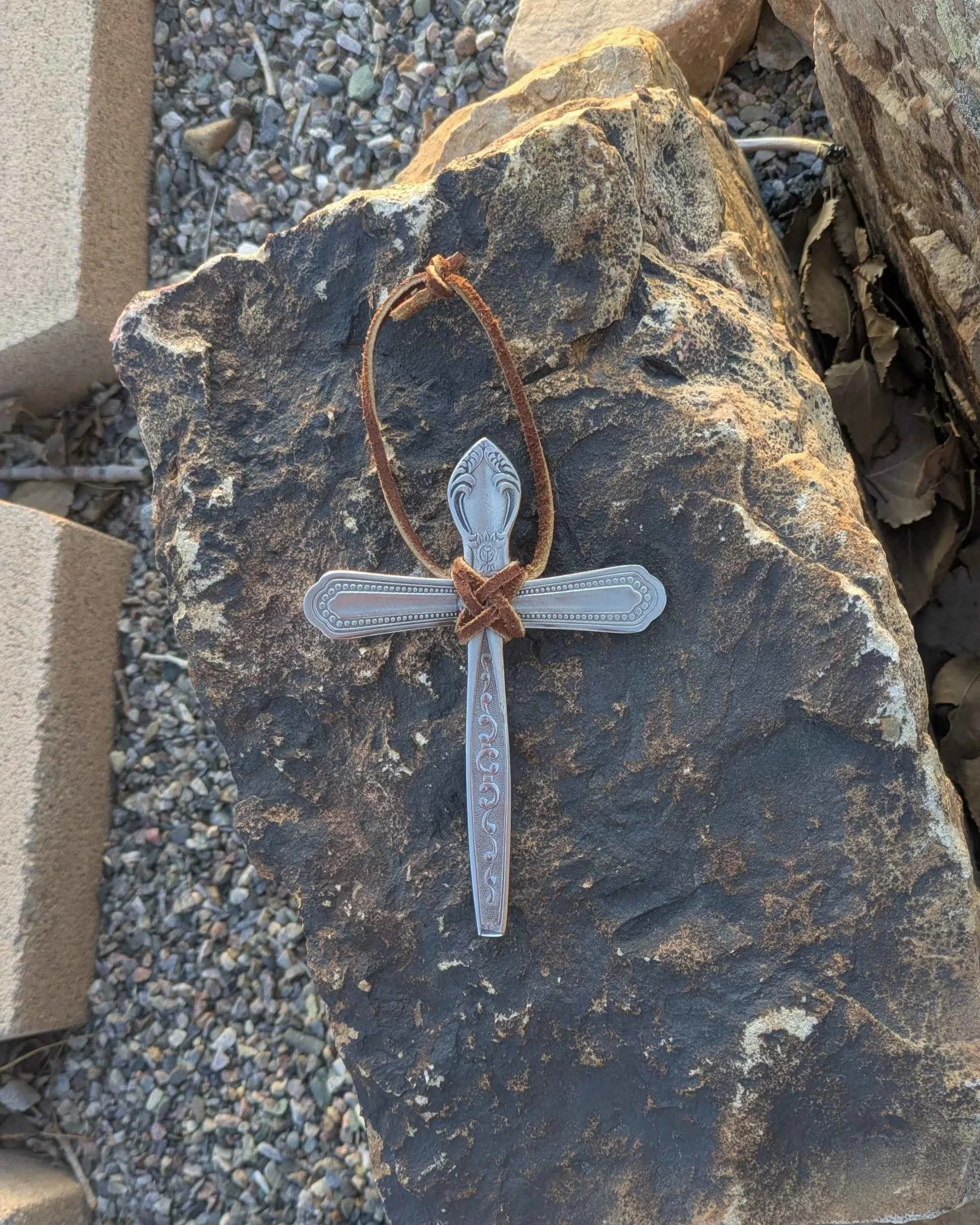 A silverware cross with an intricate leather hanging strap hung from a fence.