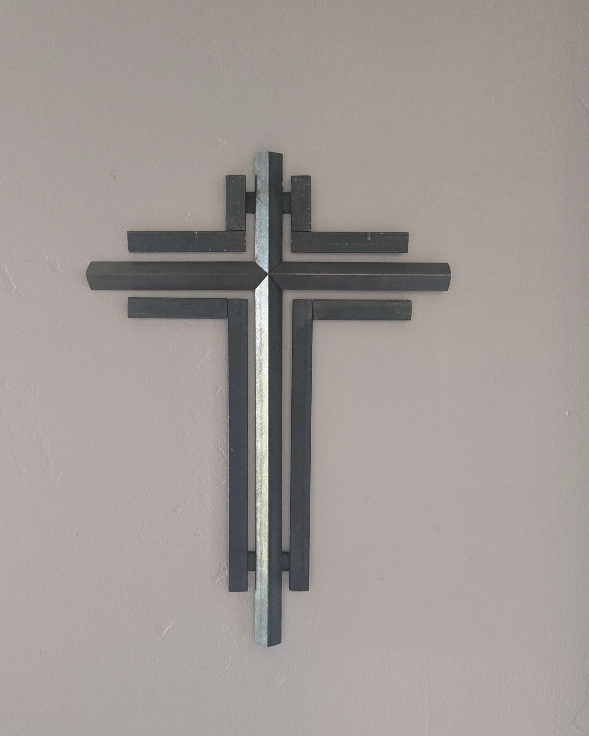 A metal art cross sculpture hung on a wall as home decor.