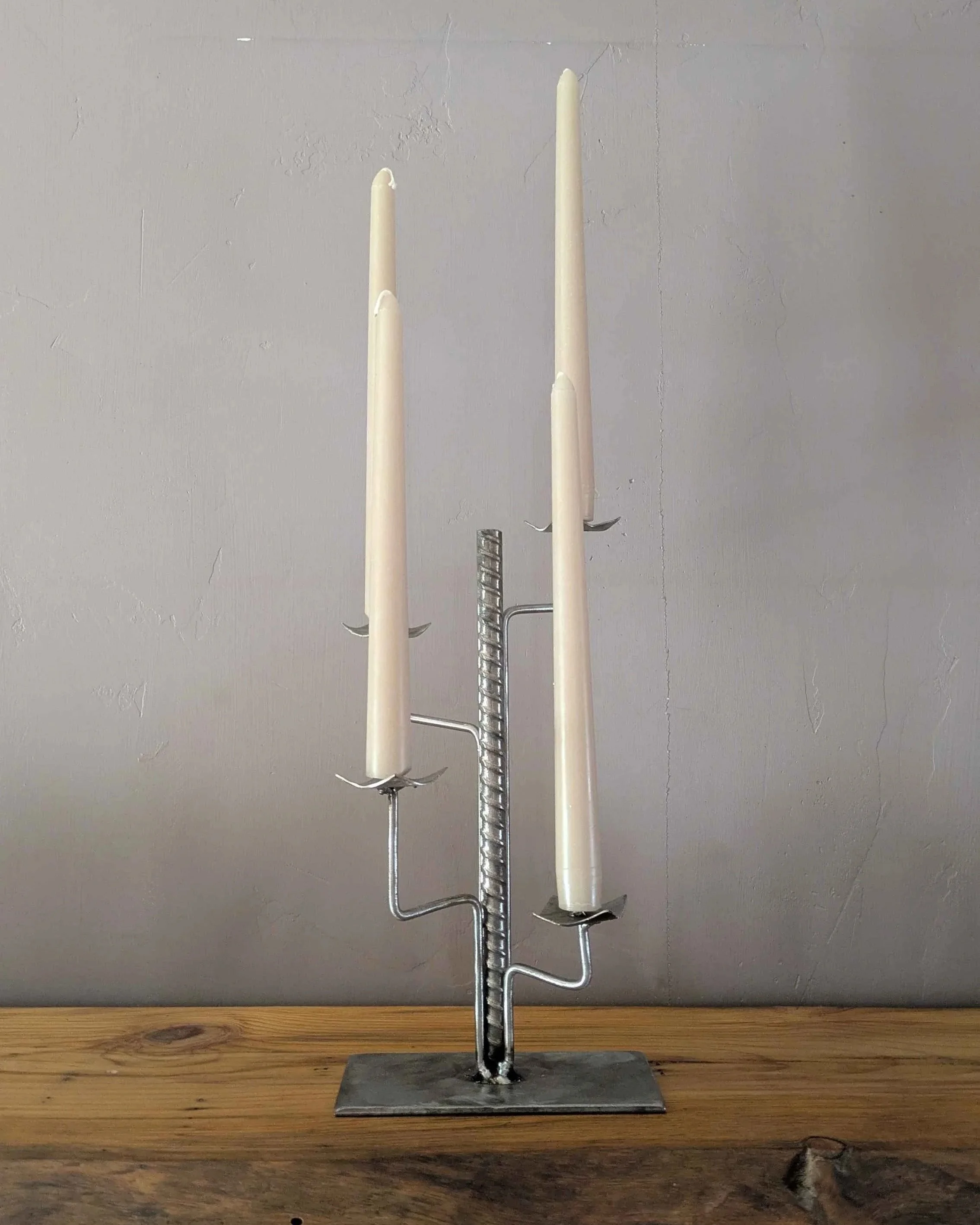 A metal art industrial style candleholder made from rebar and plate steel sitting on a shelf.