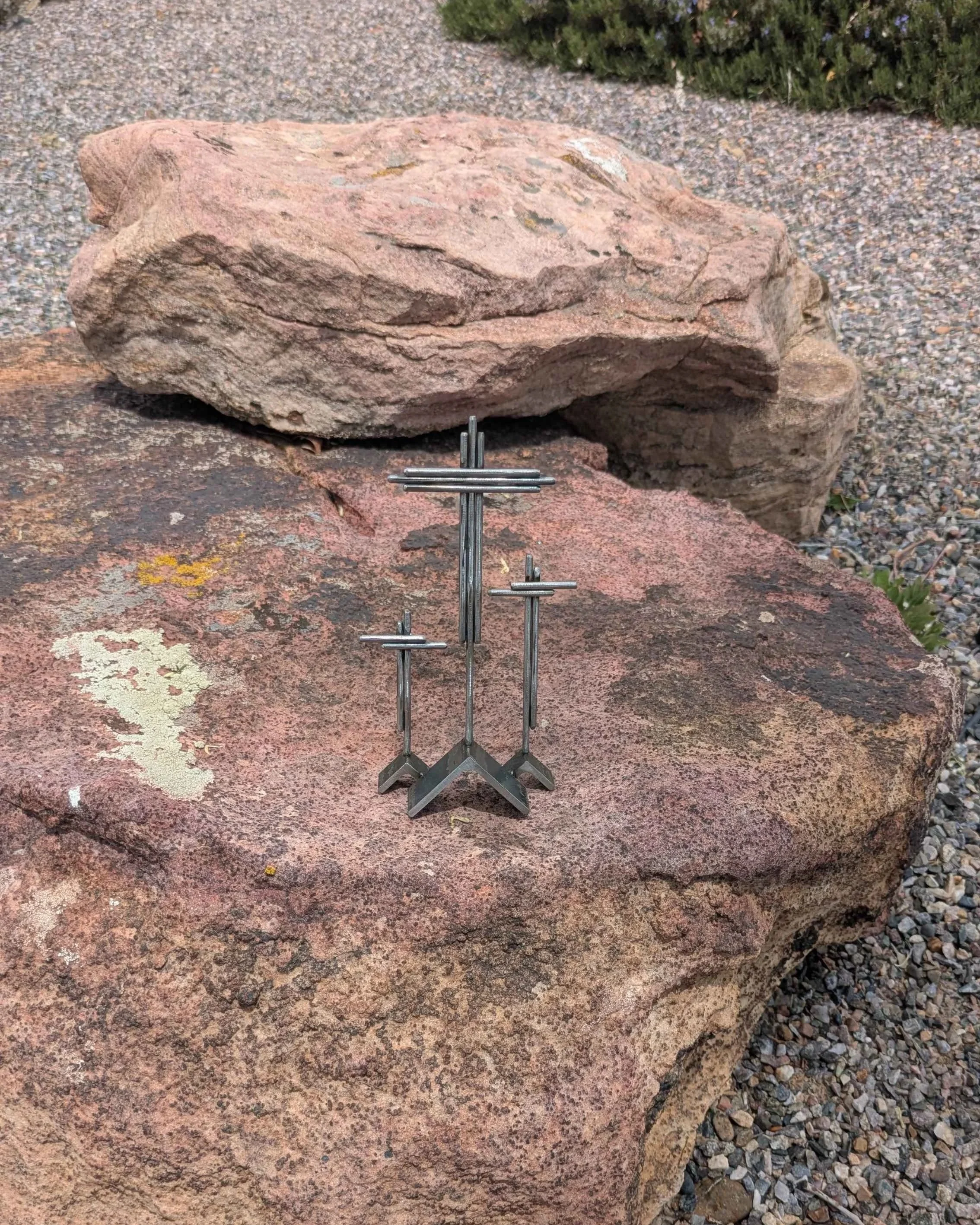 A metal art display of three crosses on three hills, made from rods and angle iron.