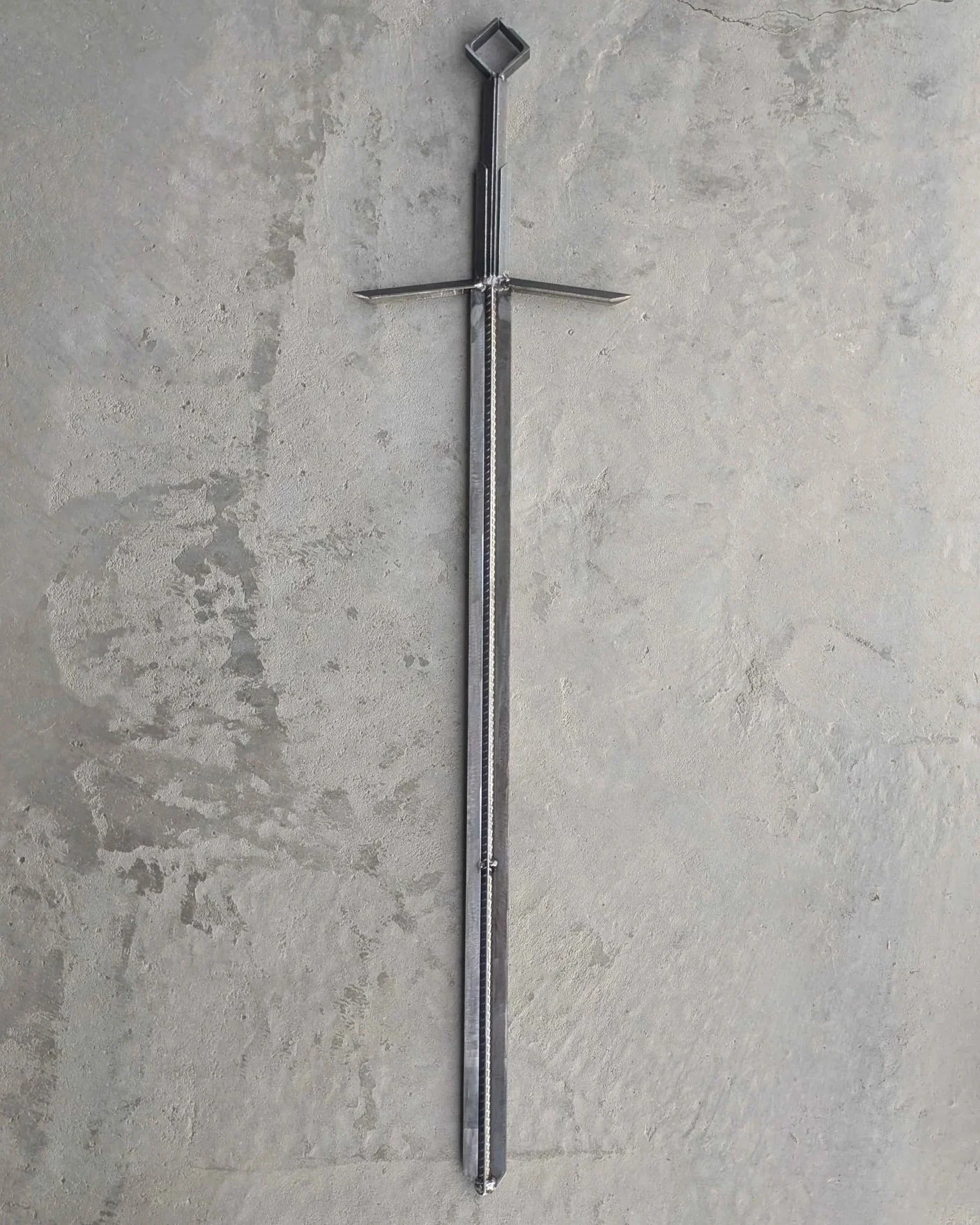 A metal art sword made from industrial style materials, laying upon concrete.