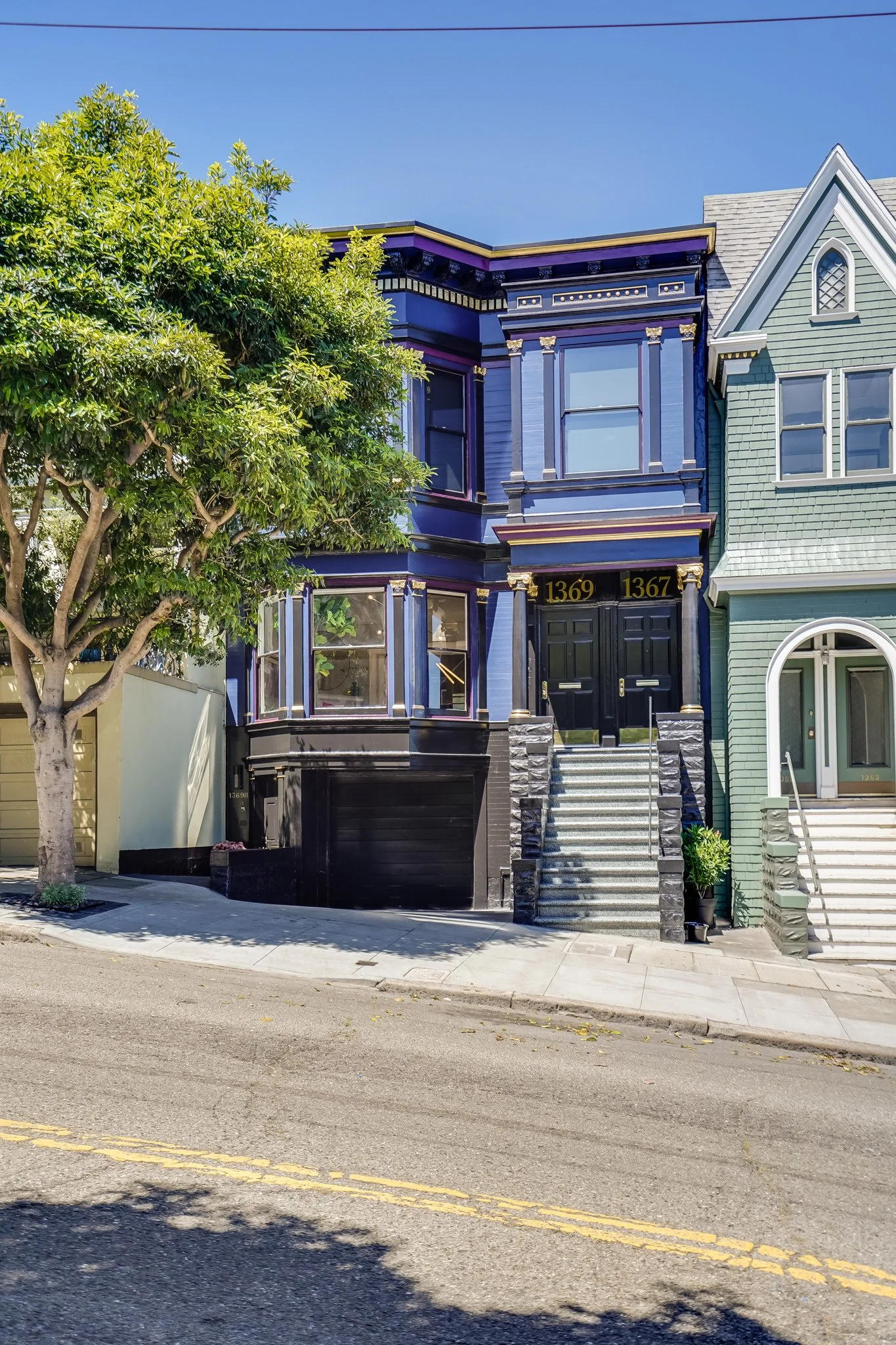 A row of victorian houses on a Haight-Ashbury street with a tree in front and a blue sky overhead.