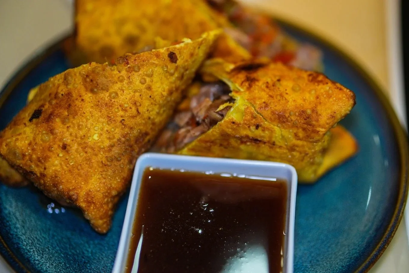 Two crispy egg rolls on a blue plate with a small white dish of dark soy sauce in front.