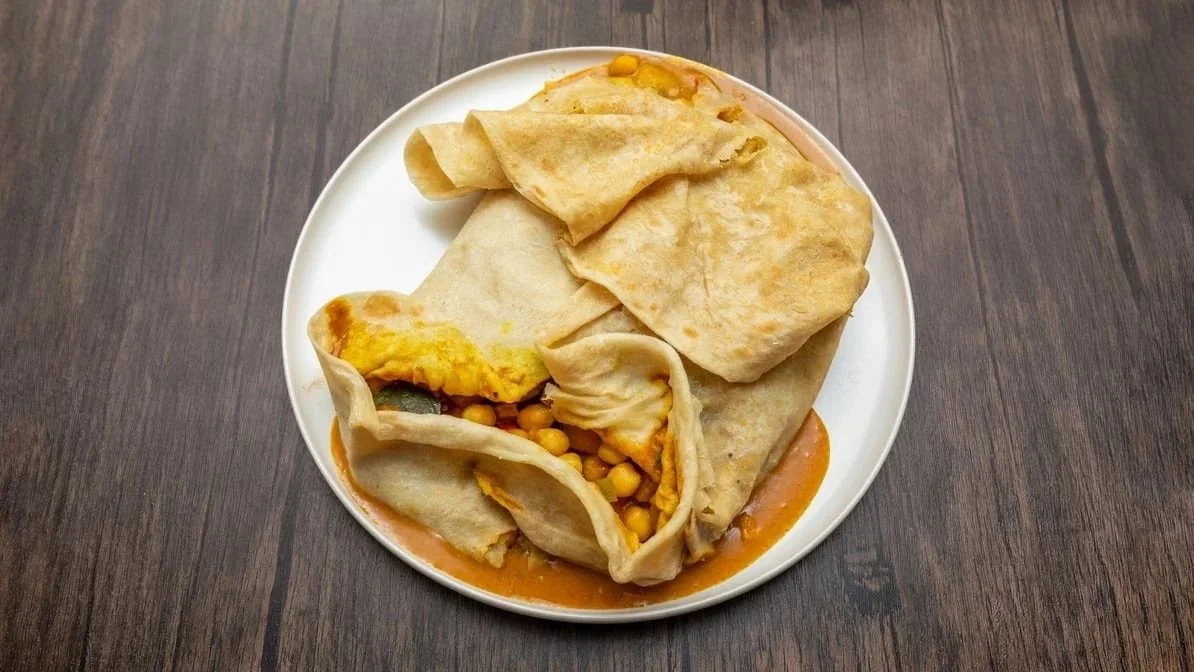 Plate with several folded crispy crepes filled with scrambled eggs, corn, and vegetables, served with tomato sauce on a dark wooden table.