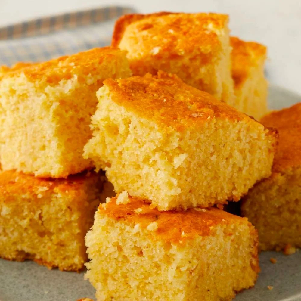 Close-up of several pieces of golden yellow cornbread with a crispy top, stacked on a plate.