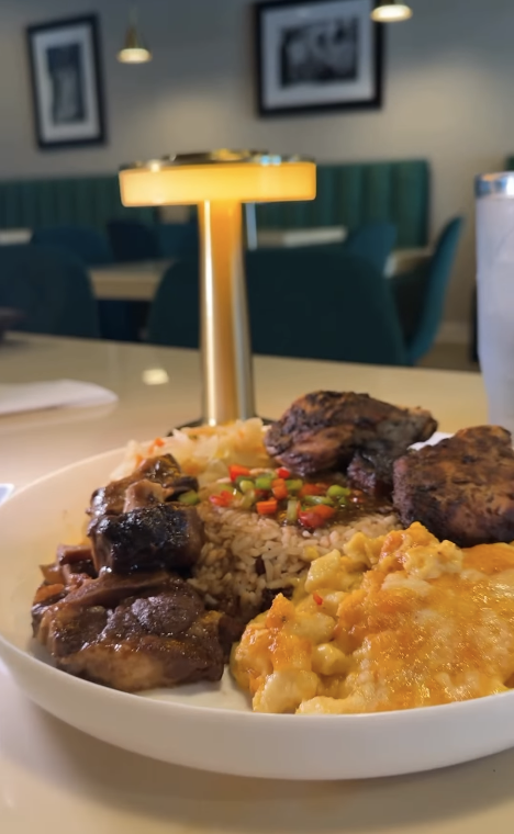 A plate of food with rice, mashed potatoes with cheese, and grilled meat, on a dining table in a restaurant with teal booths and framed pictures on the wall.