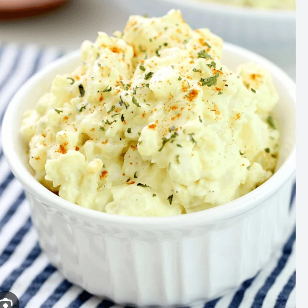 A bowl of mashed potatoes garnished with chopped herbs and paprika.