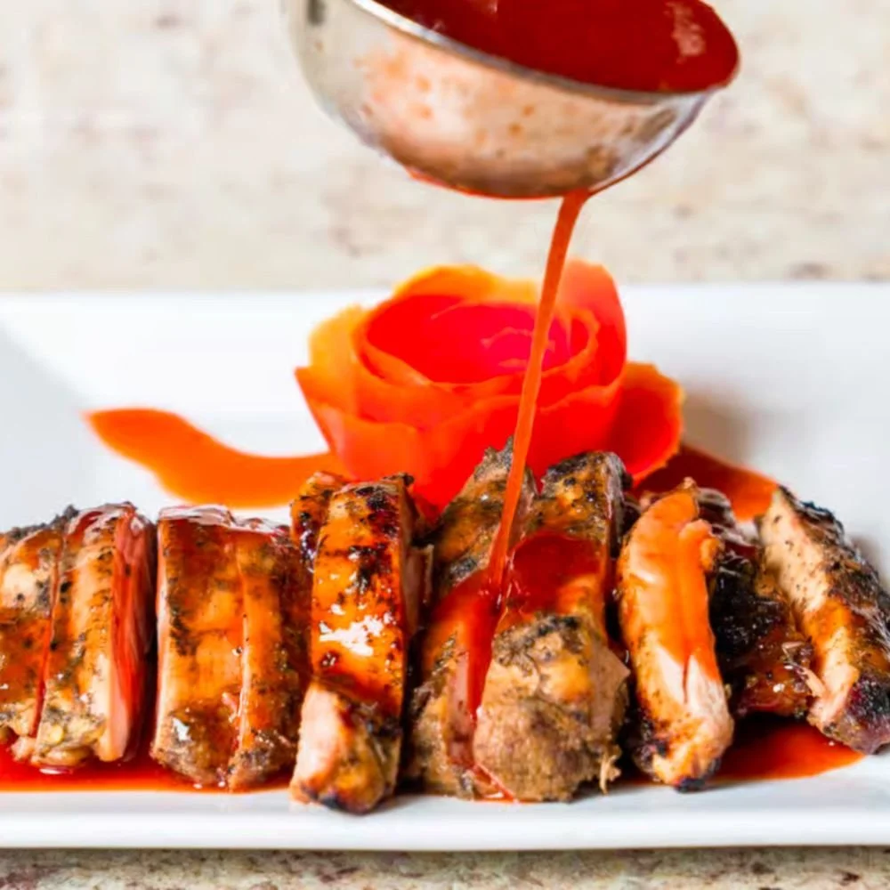 Barbecue ribs with sauce being poured over them, garnished with a rose-shaped carrot decoration on a white plate.