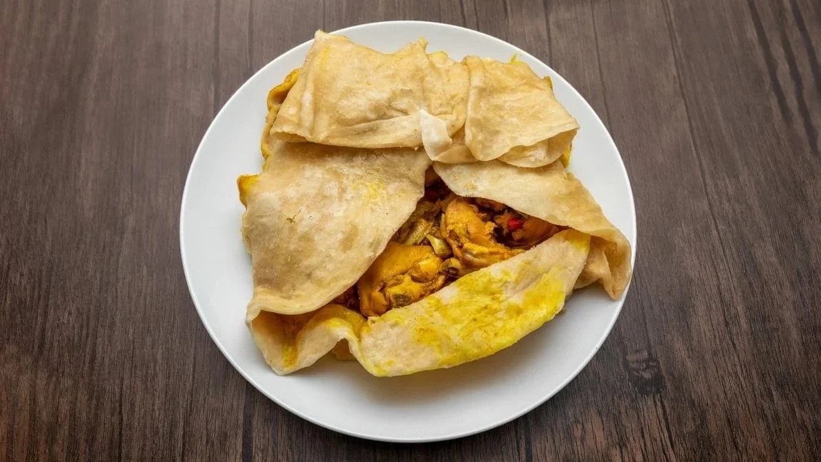 A white plate with a folded tortilla or flatbread partially covering a filling of chicken and vegetables, on a wooden table.