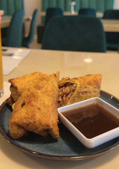Fried spring rolls with a side of dark dipping sauce on a plate in a restaurant setting.