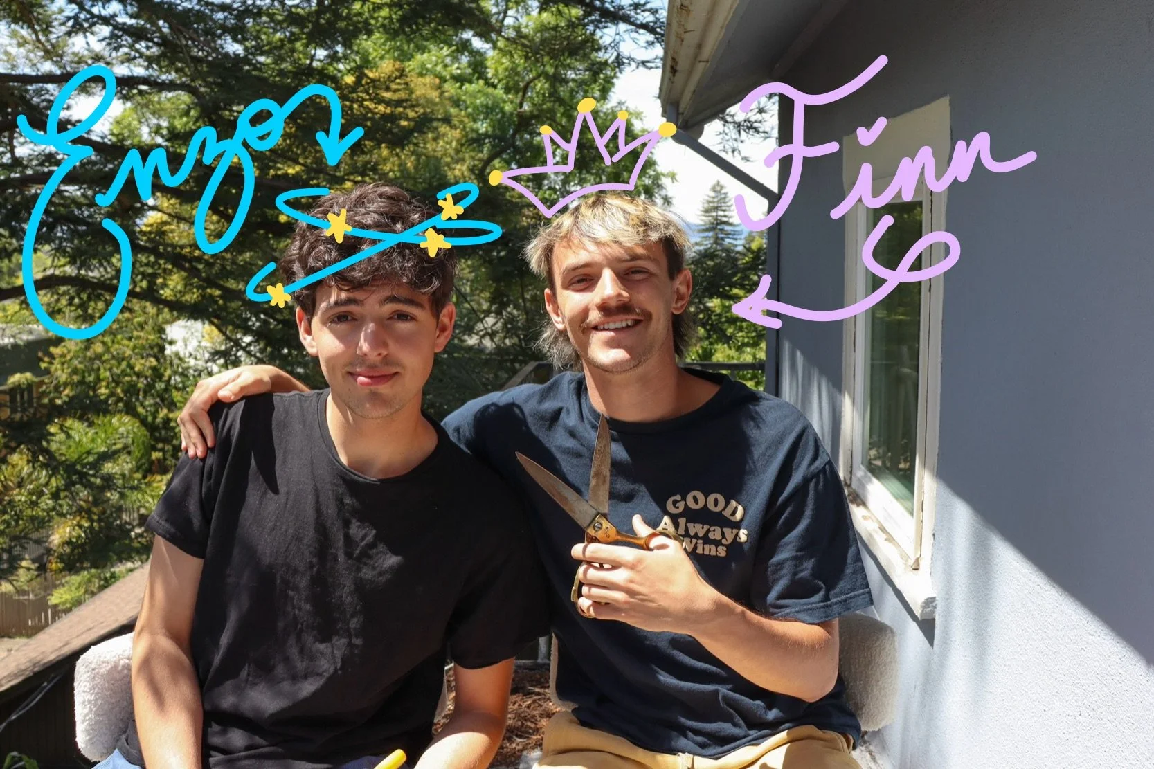 Two young men standing outside near a house, with trees in the background, smiling for a photo. One is holding a pair of scissors while the other has his arm around his friend’s shoulder. There are handwritten annotations on the image that say 'Emz' with a small star and a crown, and 'Fin' with an arrow.