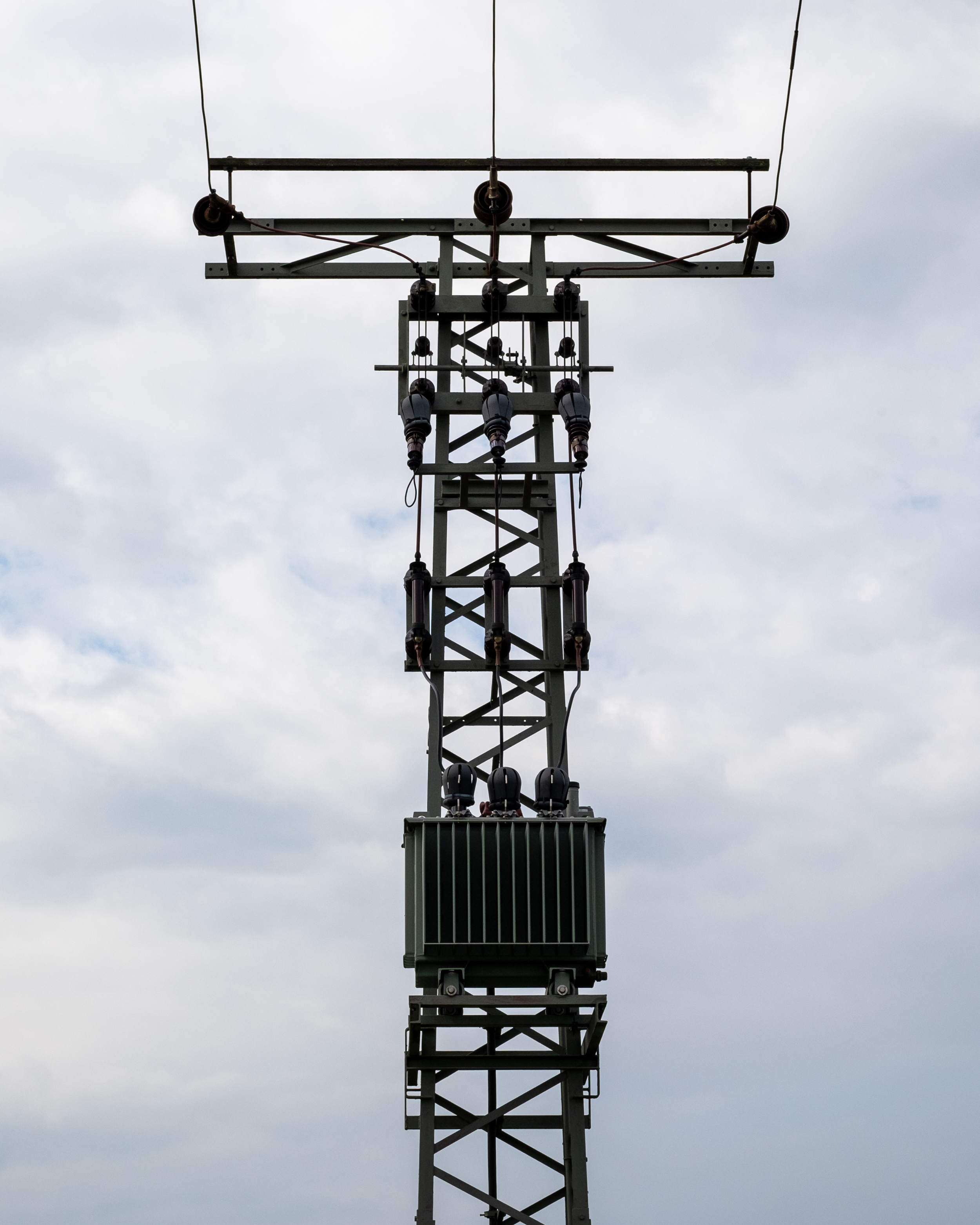 Torre eléctrica con estructura metálica y aisladores, bajo un cielo nublado.