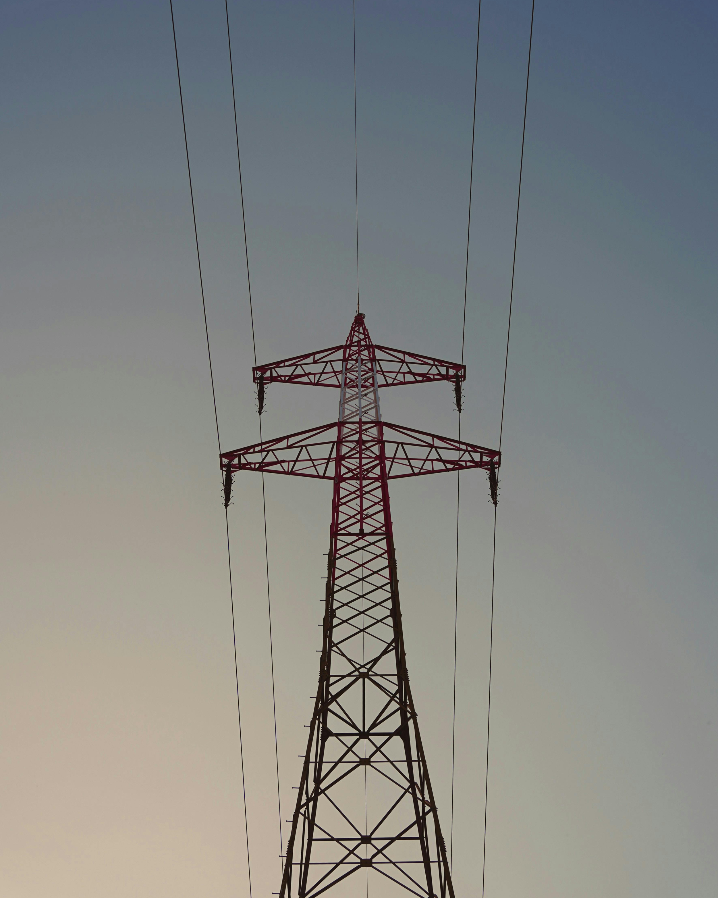 Vista de una torre de transmisión eléctrica de metal pintada de rojo y blanco, con cables en el cielo en el fondo.