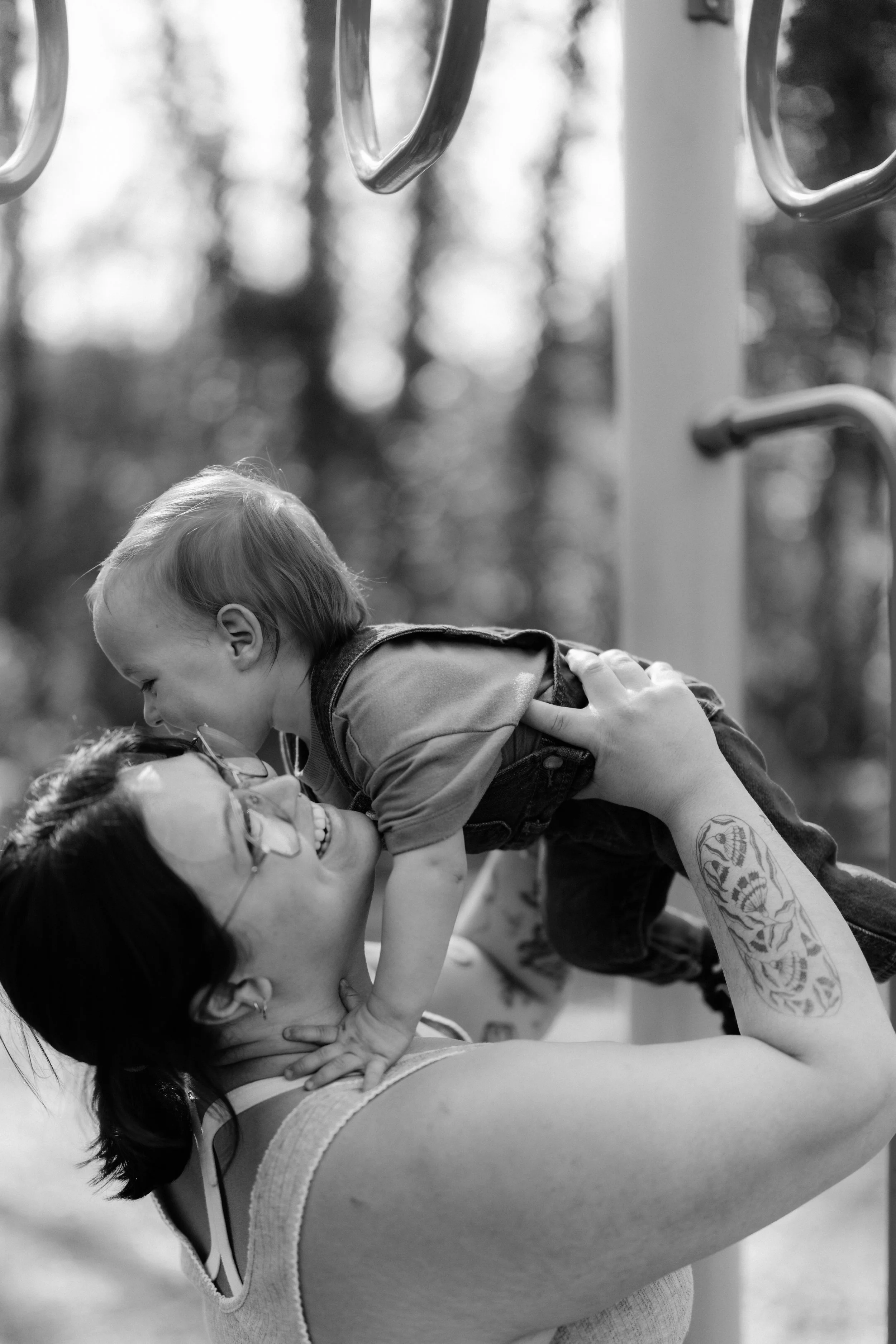 A woman lifts her toddler over her head, both are smiling, on playground setting