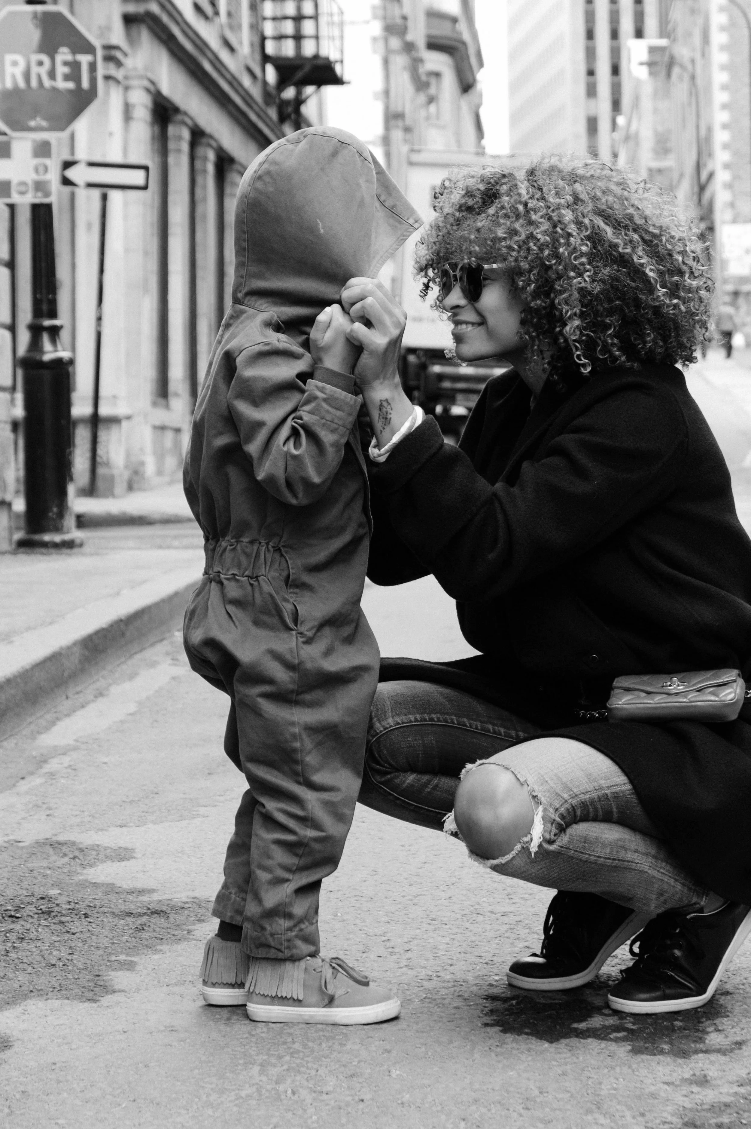 A mother squats down to look her child in the eyes, in an urban setting