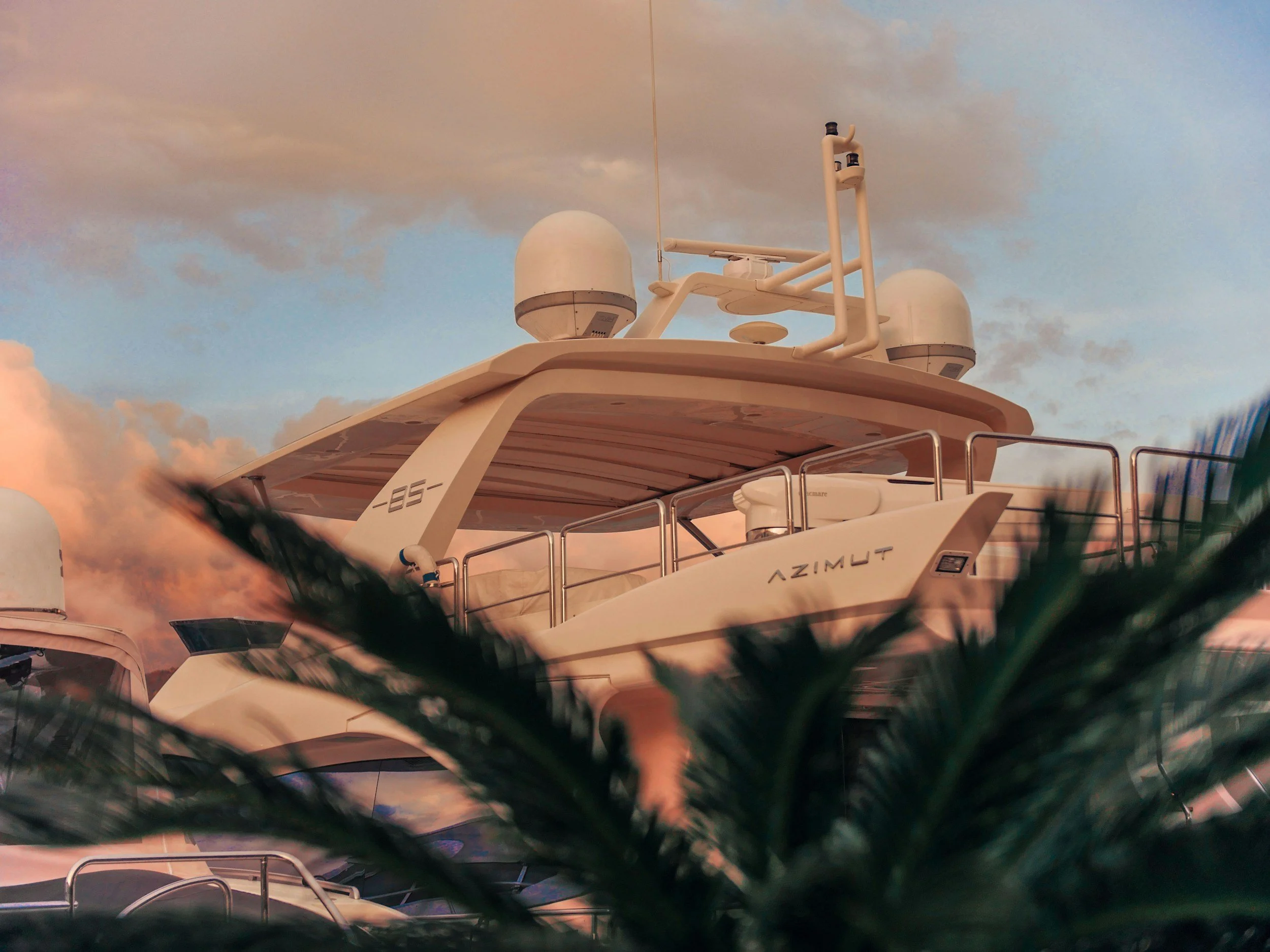 The top part of a white yacht boat with radar and communication equipment mounted on the roof against a cloudy sky during sunset.