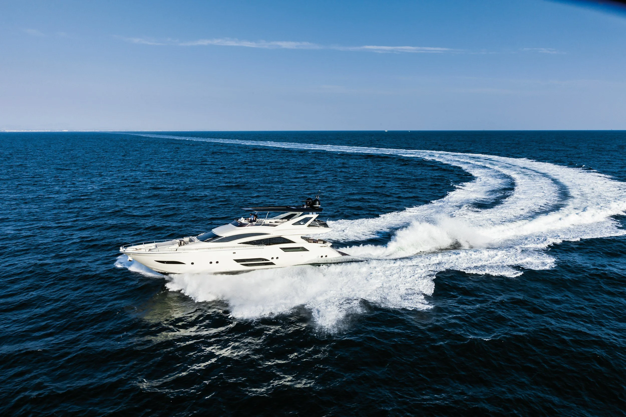 A white yacht moving across the ocean, leaving a wake behind it under a clear blue sky.