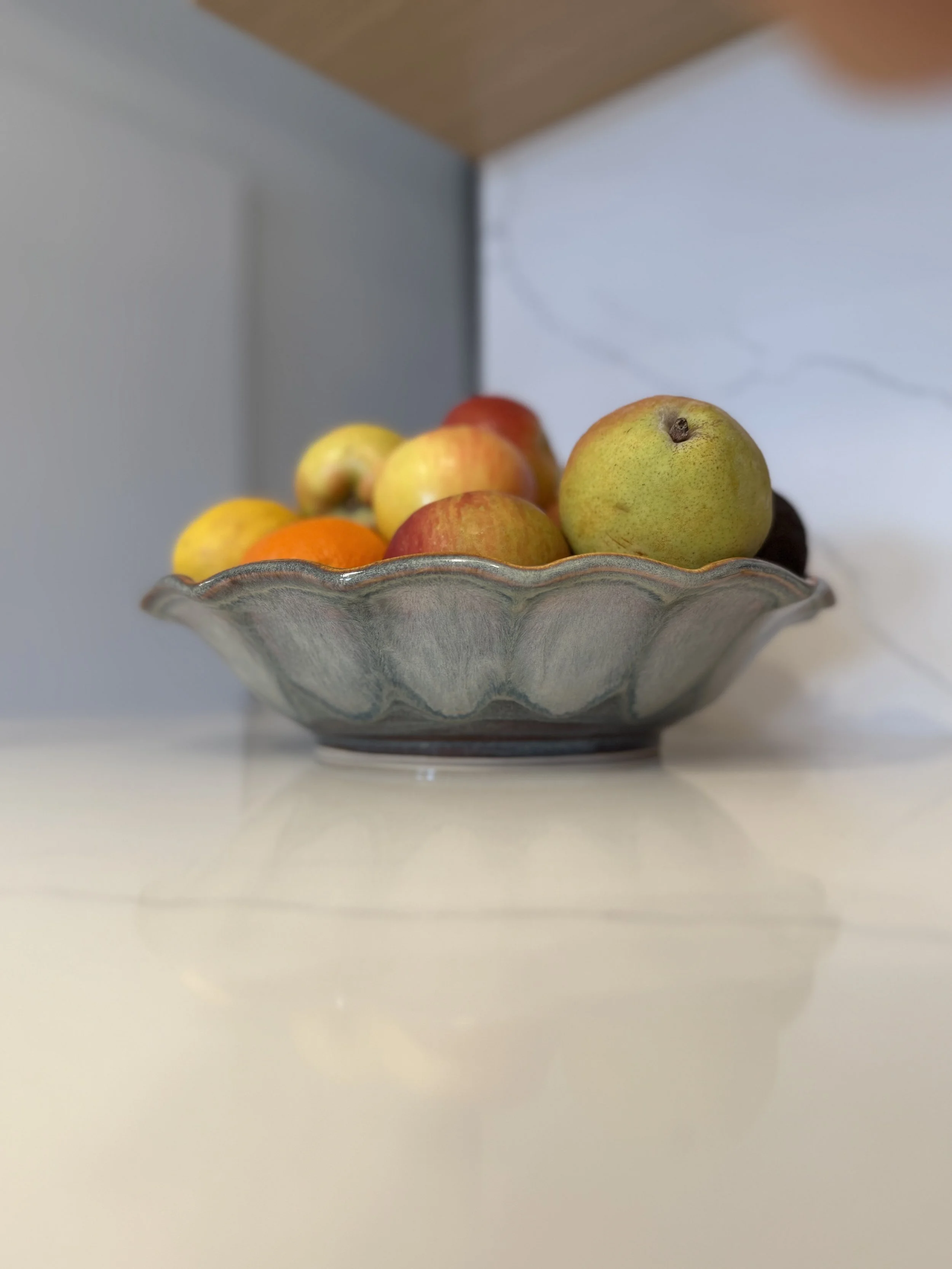 A decorative ceramic bowl filled with assorted small apples and fruit, placed on a white surface with a light background.