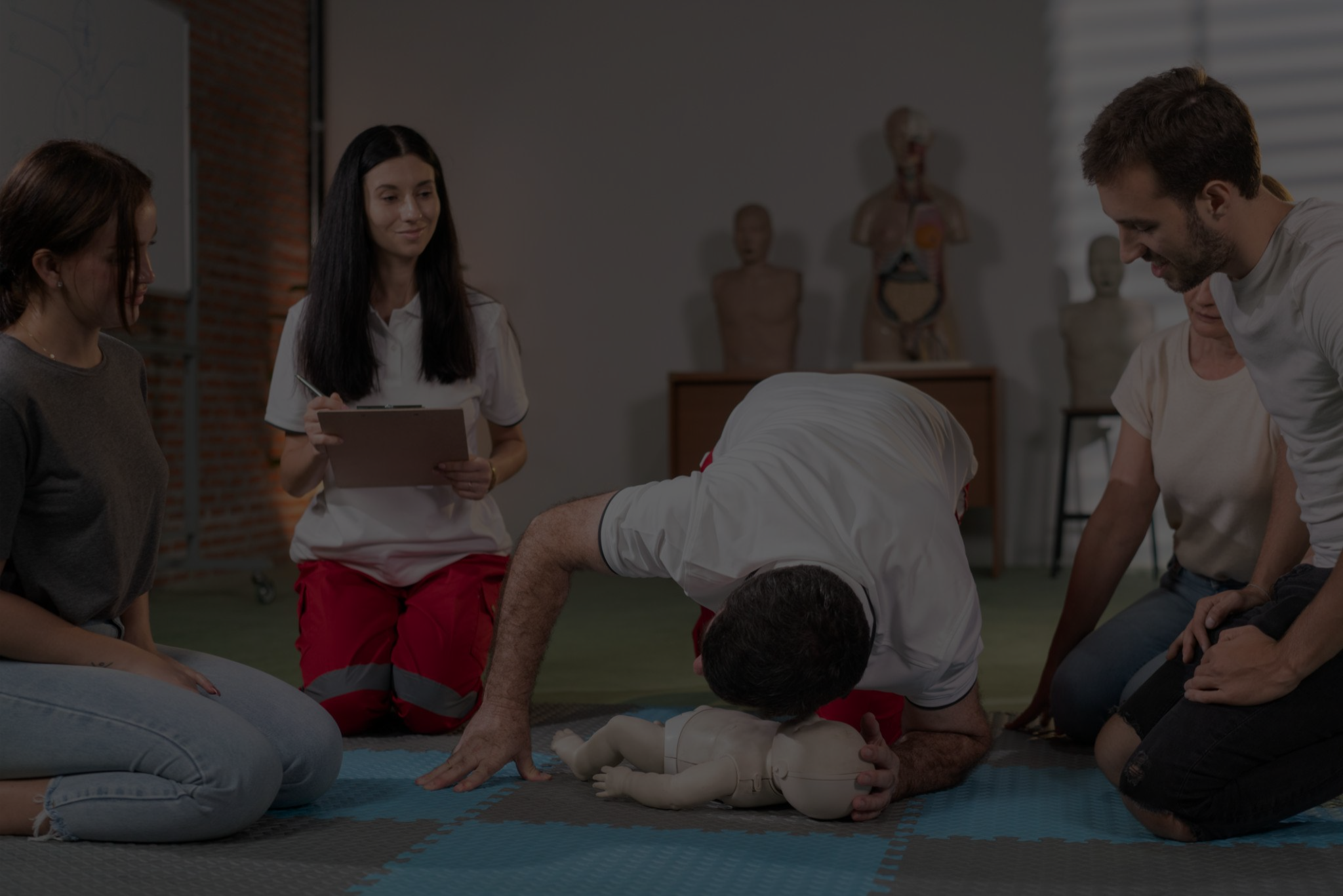 A group of people practicing CPR on a training manikin during a CPR training session in a room with anatomical models in the background.