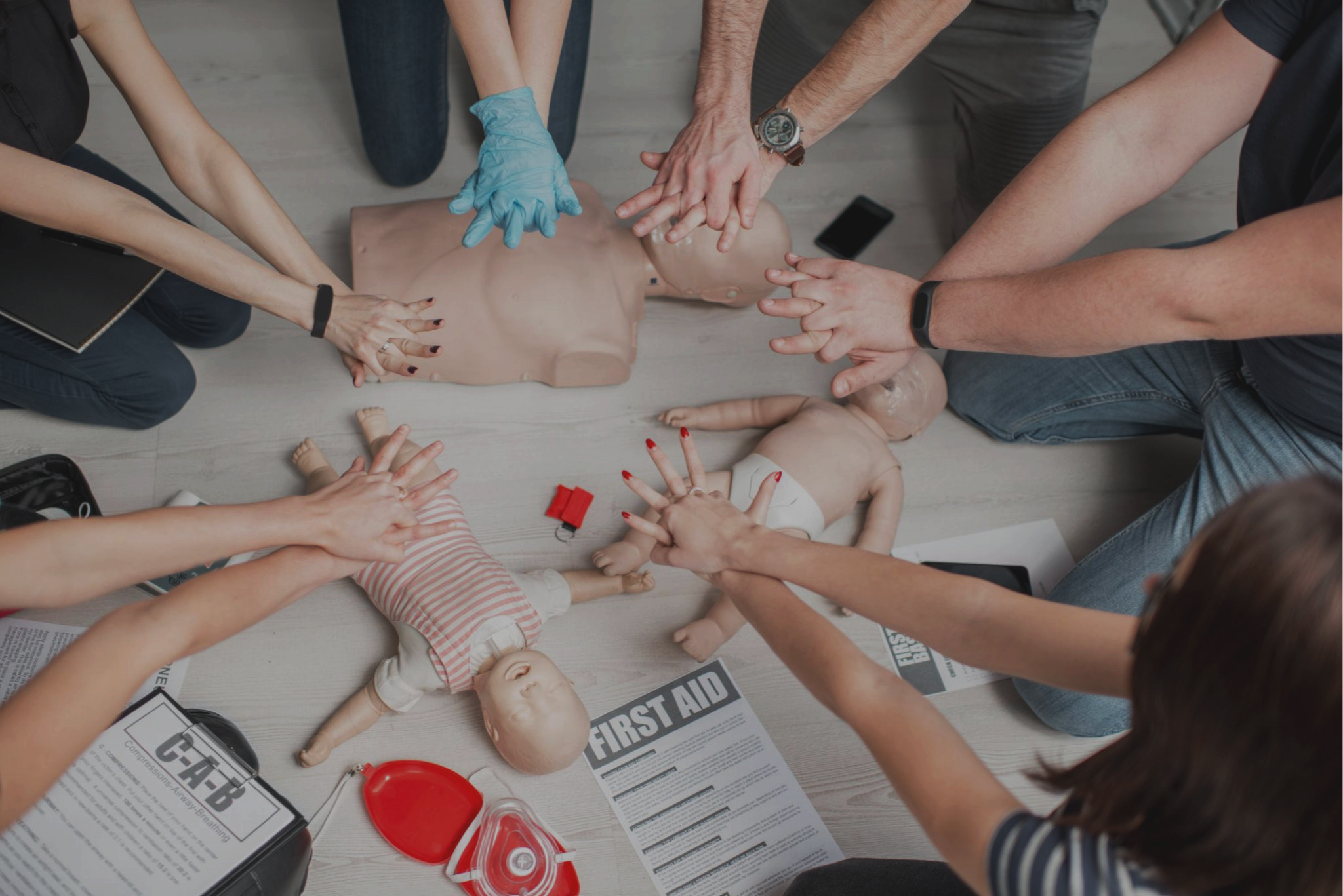 Group of people practicing CPR on a mannequin, with CPR and first aid supplies on the table.