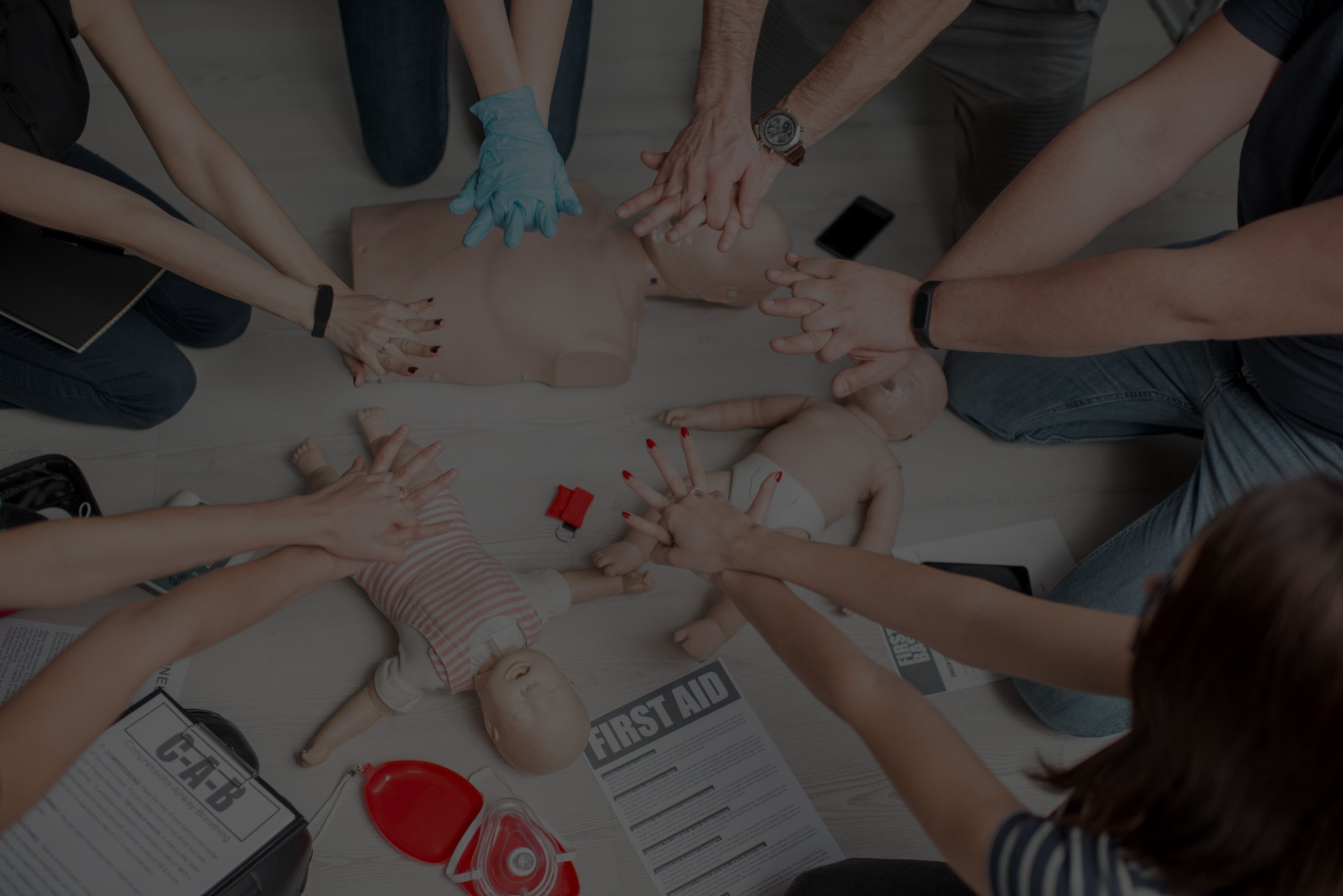 Group of people performing CPR on a training mannequin, surrounded by first aid supplies and informational pamphlets.