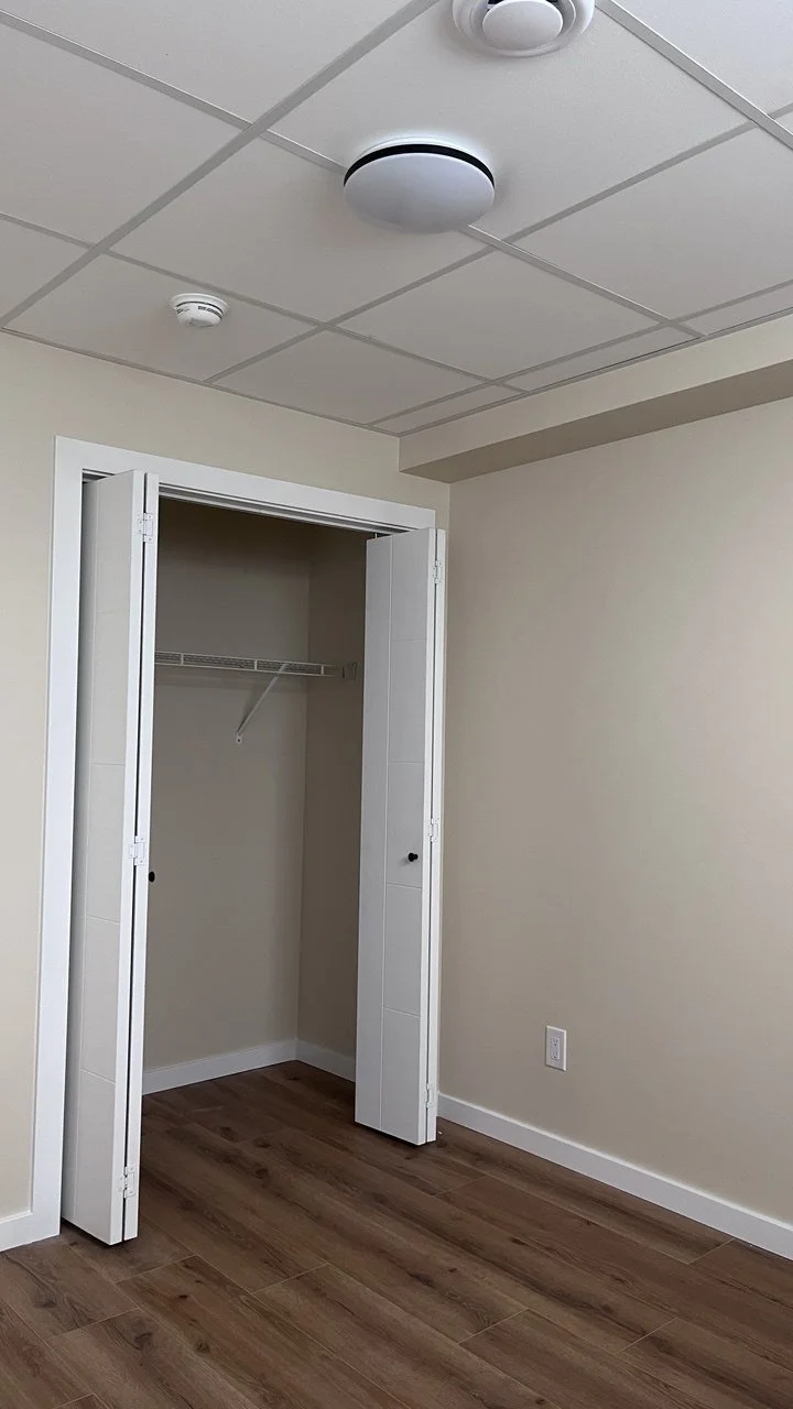 Empty closet with double doors and a wire shelf, situated in a room with beige walls, a white baseboard, and wood-finished floor.